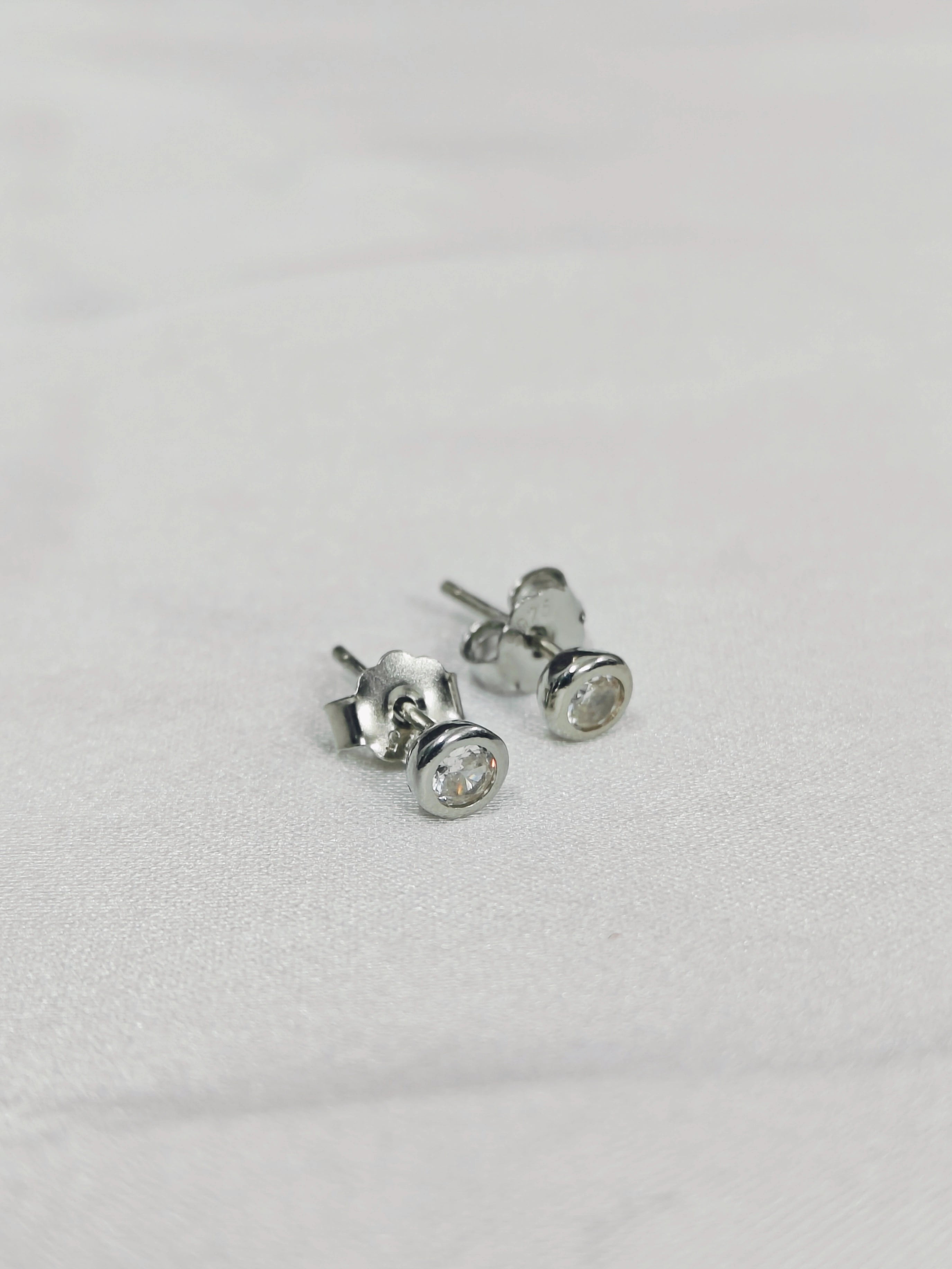 Pair of silver stud earrings with clear gemstones on a light gray background