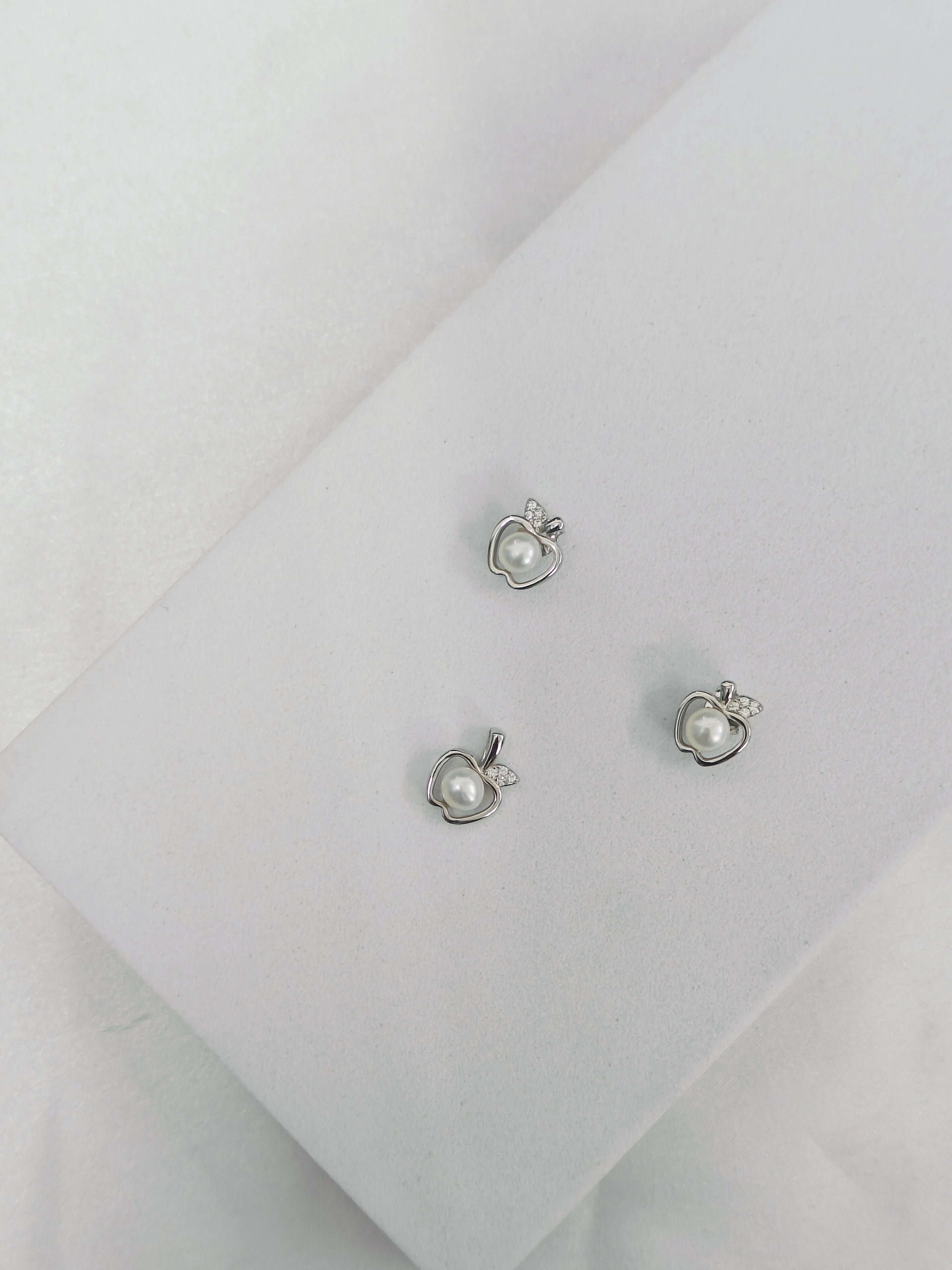 Pair of silver earrings with heart and pearl design on a light gray background