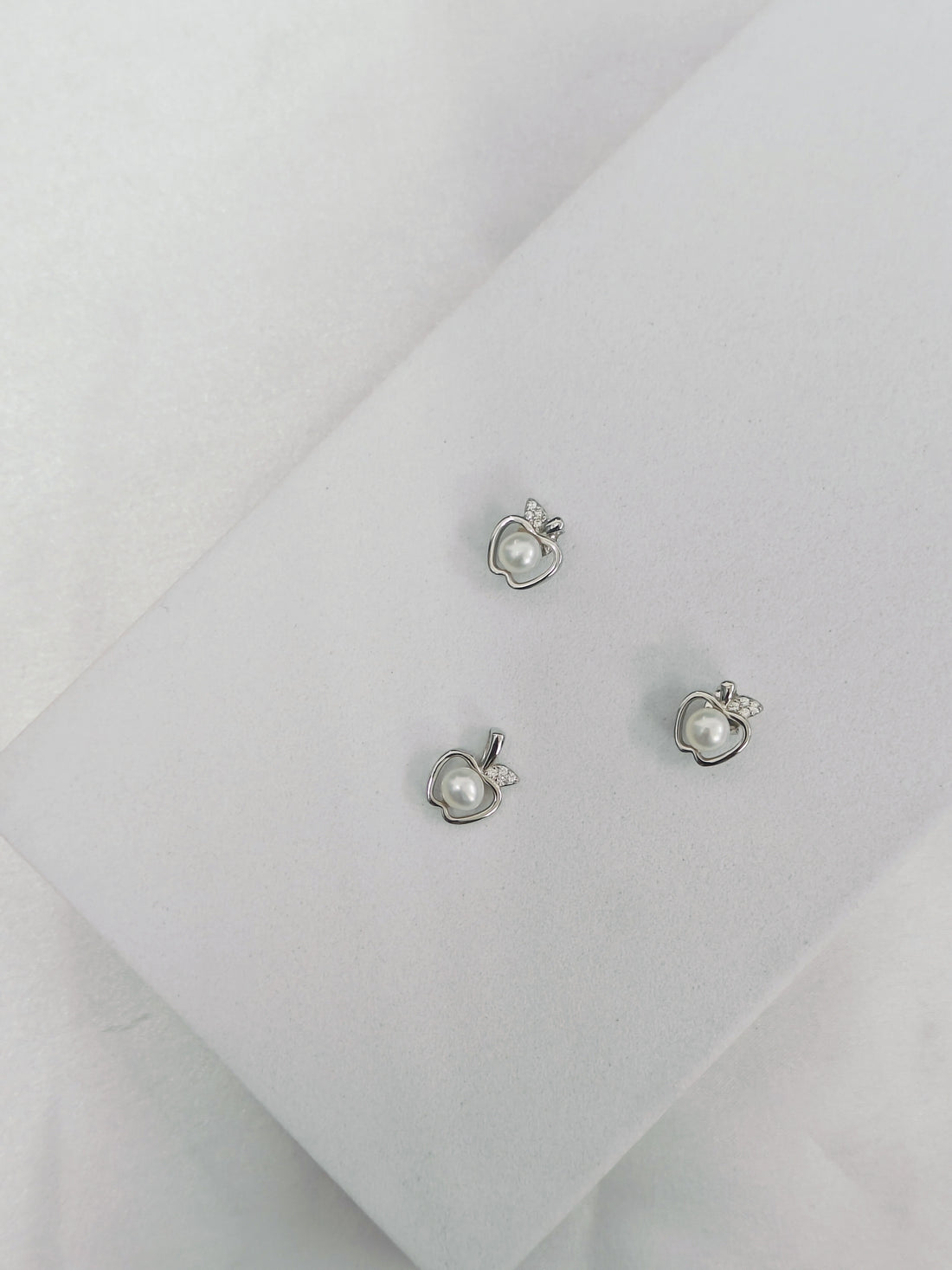 Pair of silver earrings with heart and pearl design on a light gray background