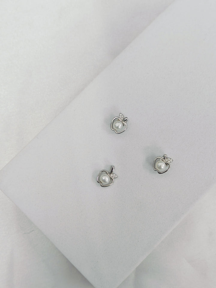 Pair of silver earrings with heart and pearl design on a light gray background
