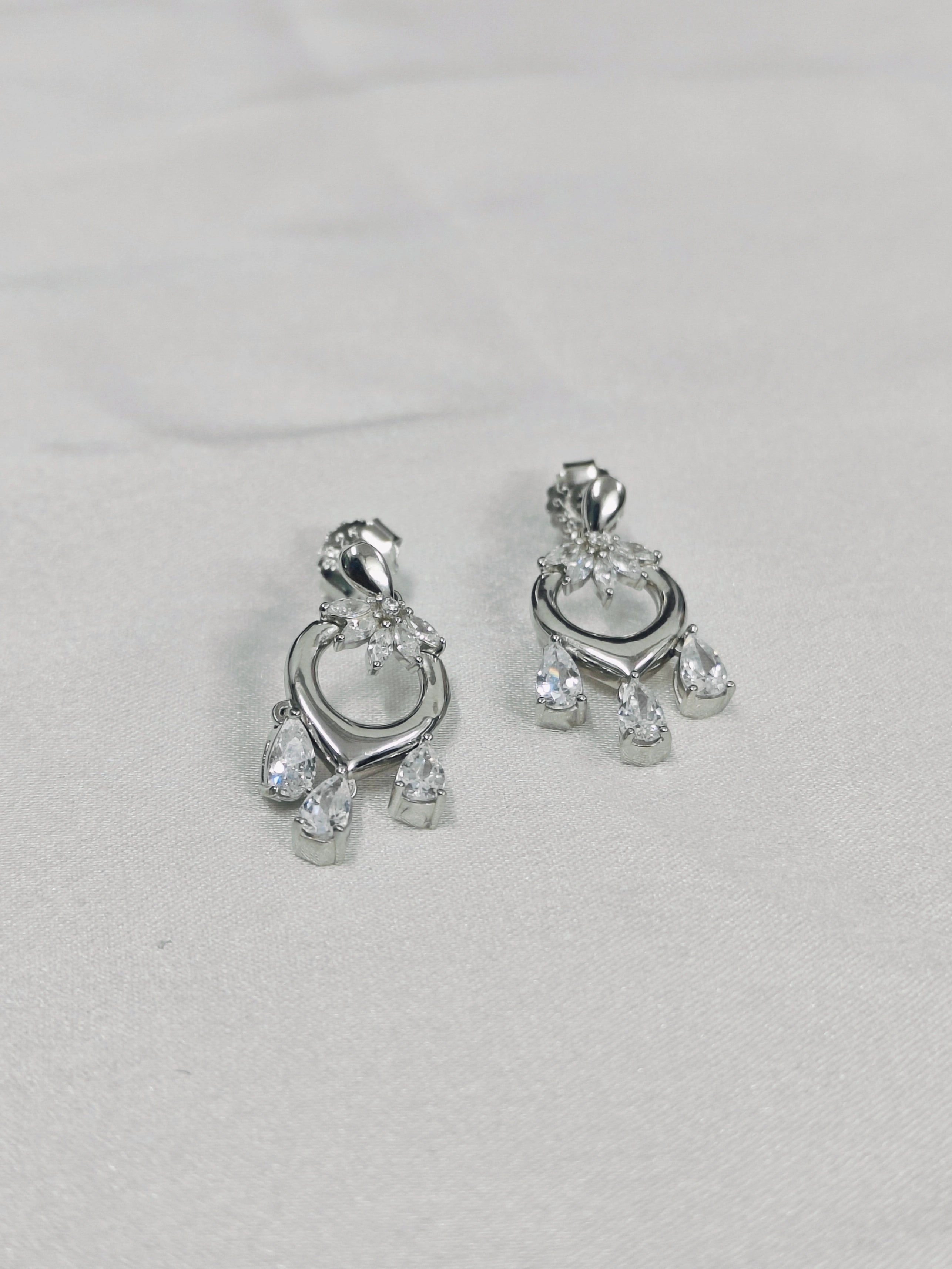 Pair of silver earrings with clear stones on a light gray background