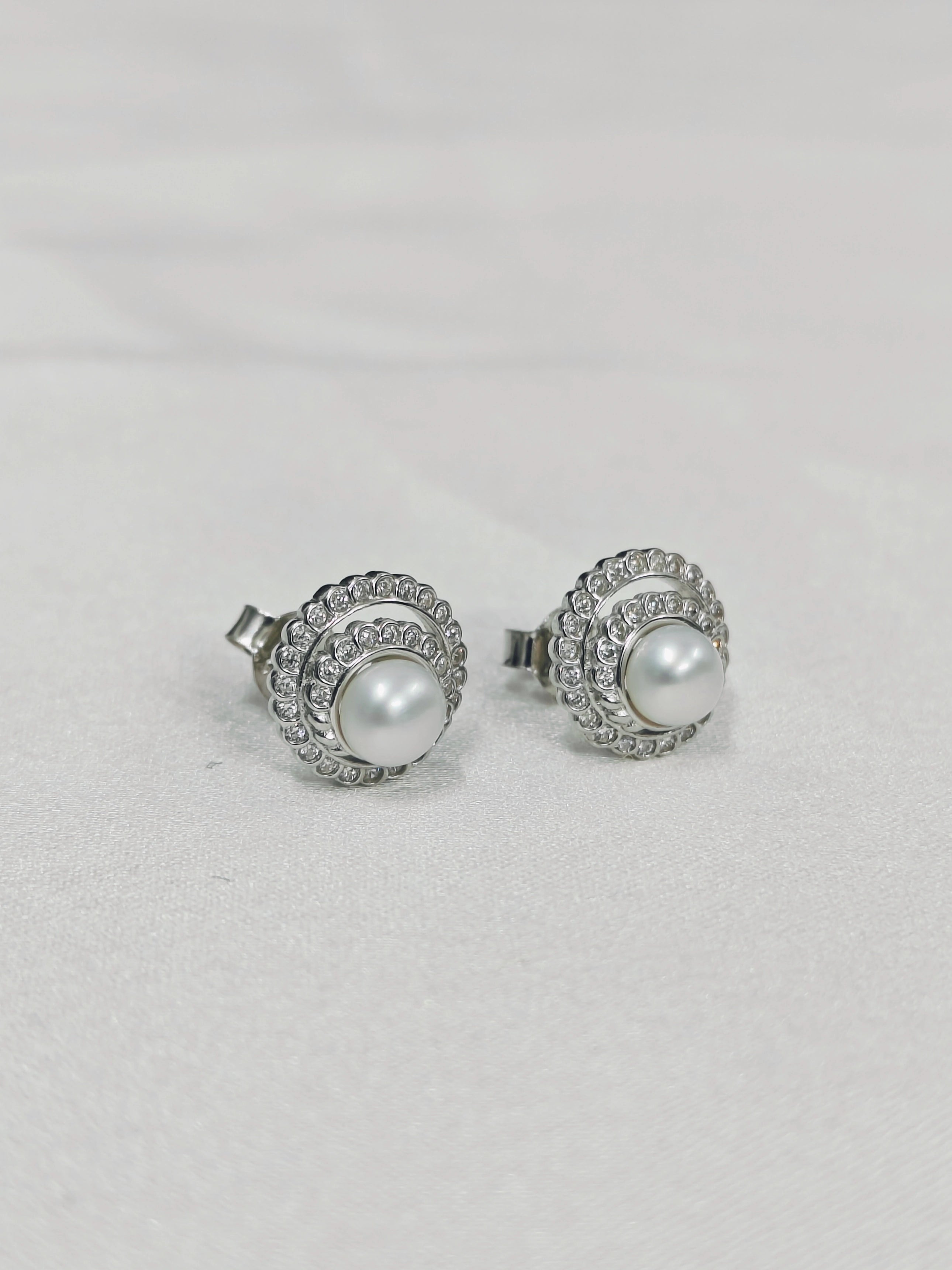 Pair of pearl stud earrings with silver embellishments on a light gray background