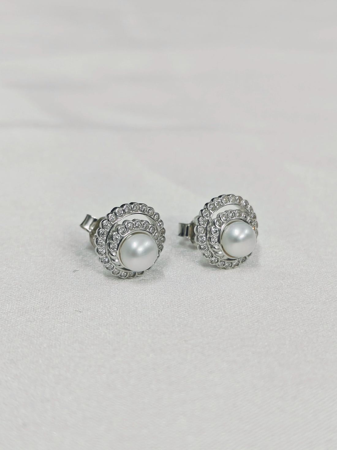 Pair of pearl stud earrings with silver embellishments on a light gray background
