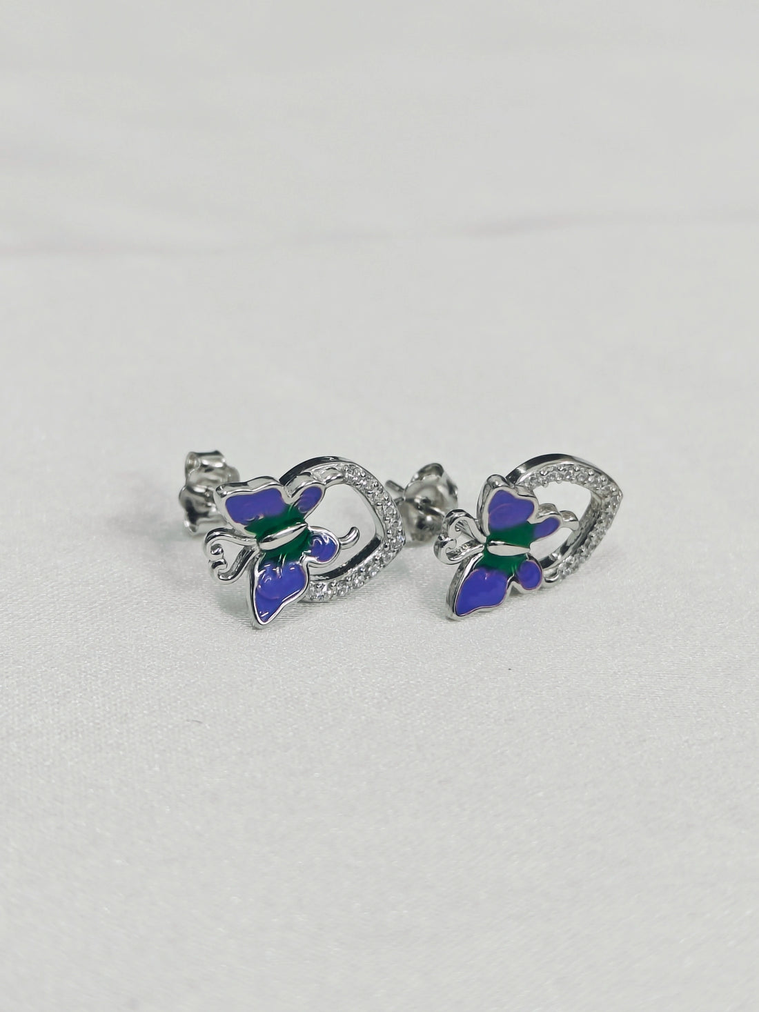 Butterfly-shaped earrings with blue and green details on a light gray background