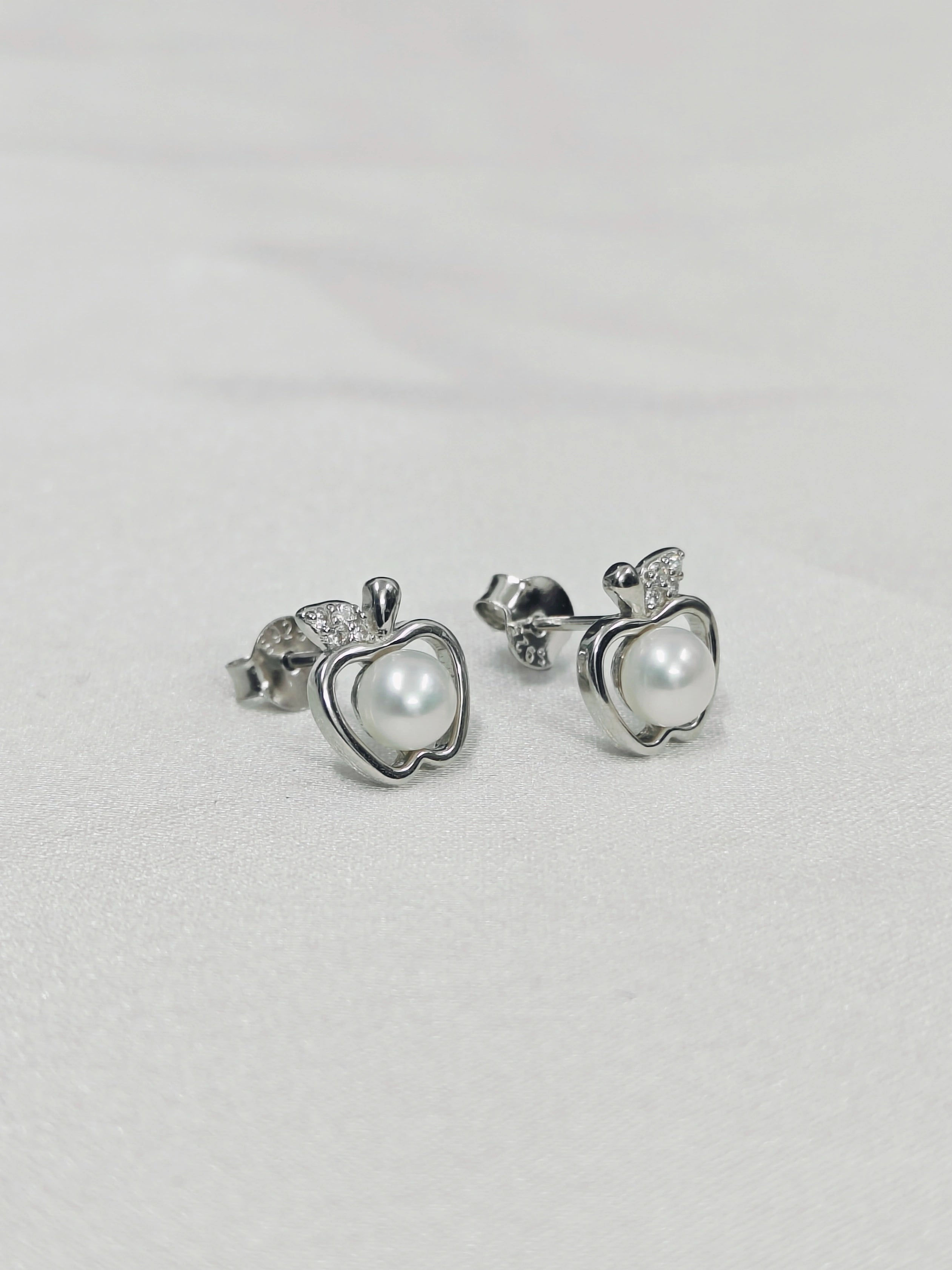 Silver earrings with heart-shaped pearl-like centers on a light gray background
