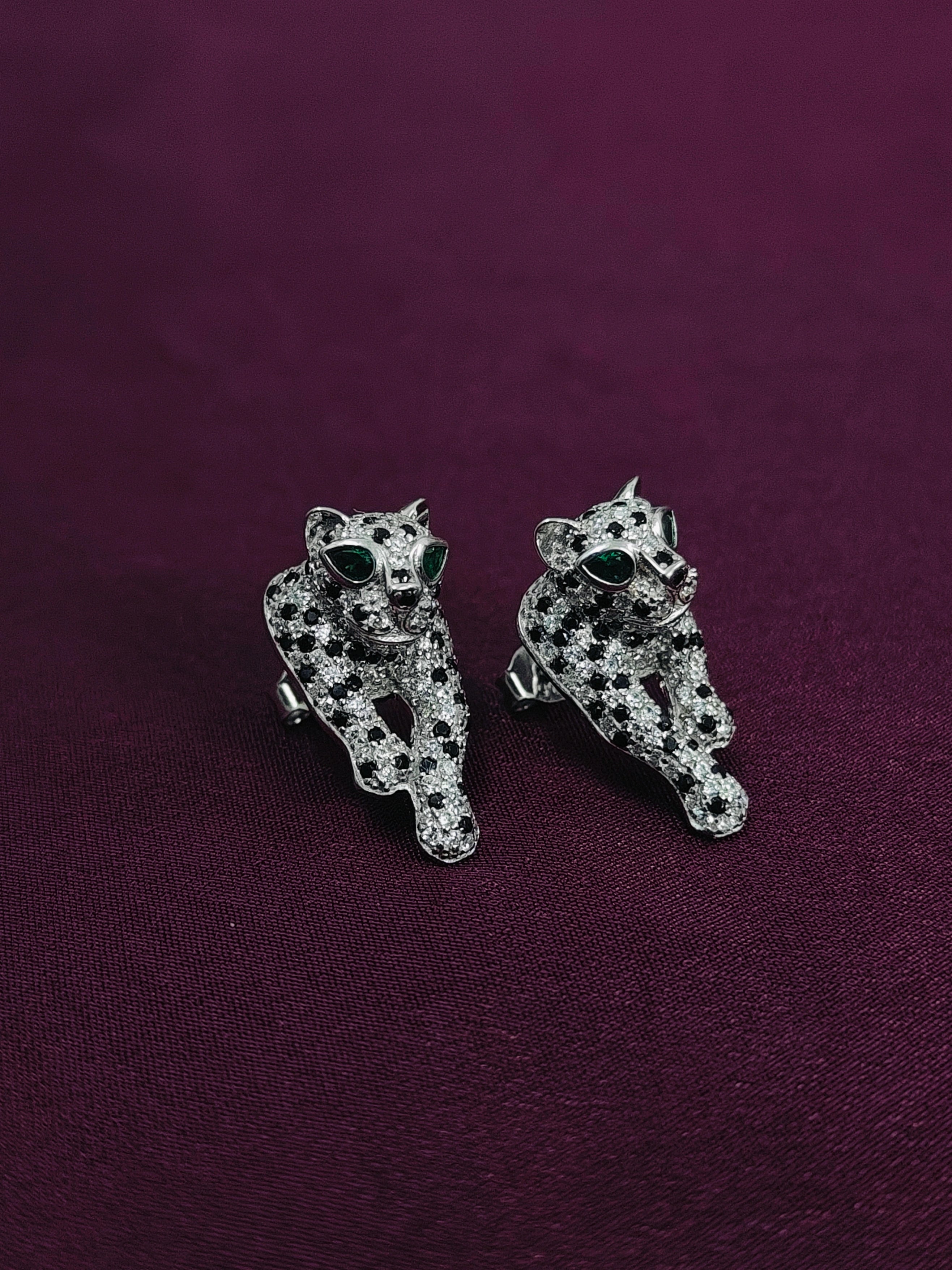 Pair of silver panther earrings on a purple background