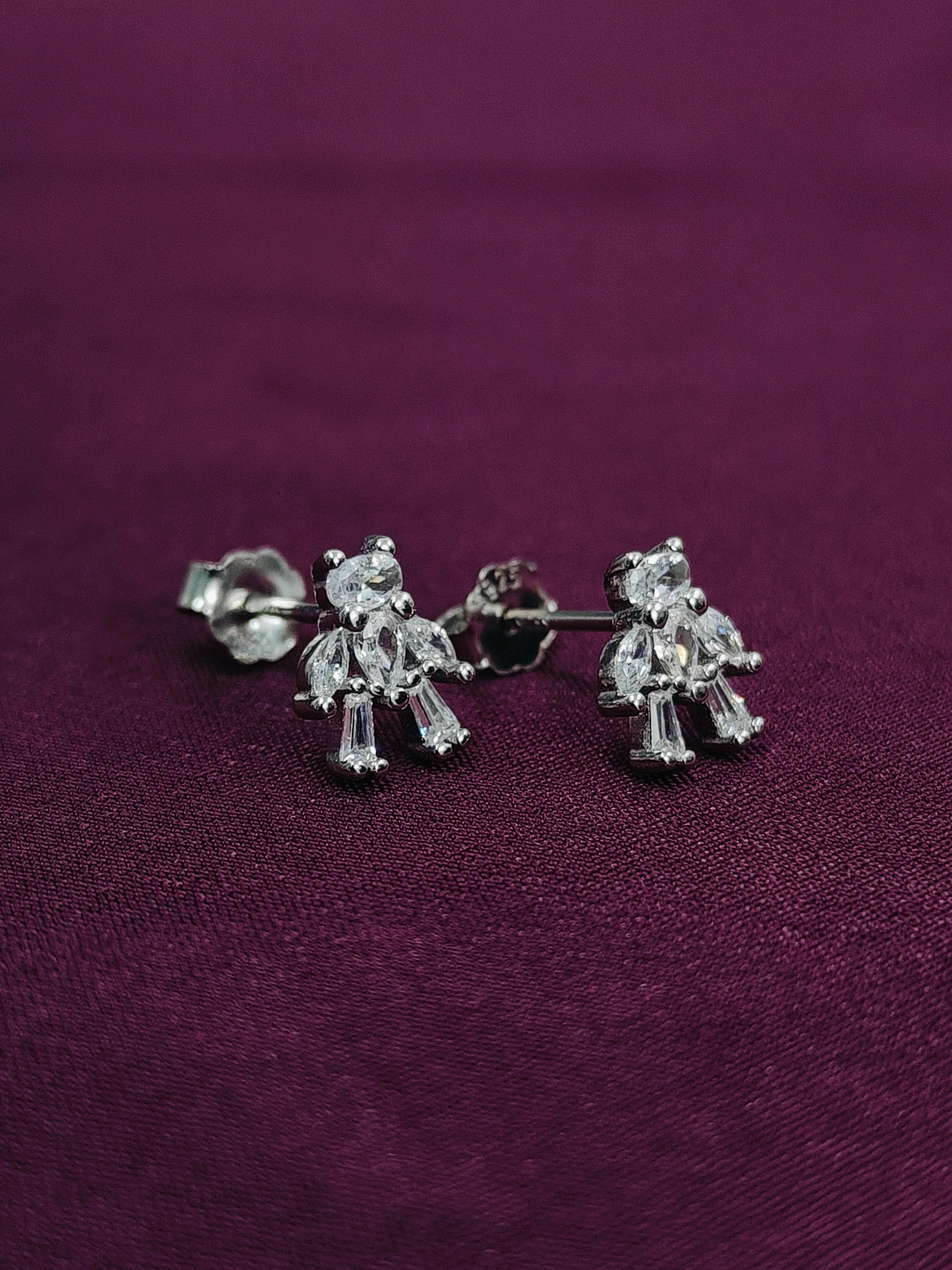 Silver teddy bear earrings on a purple fabric background