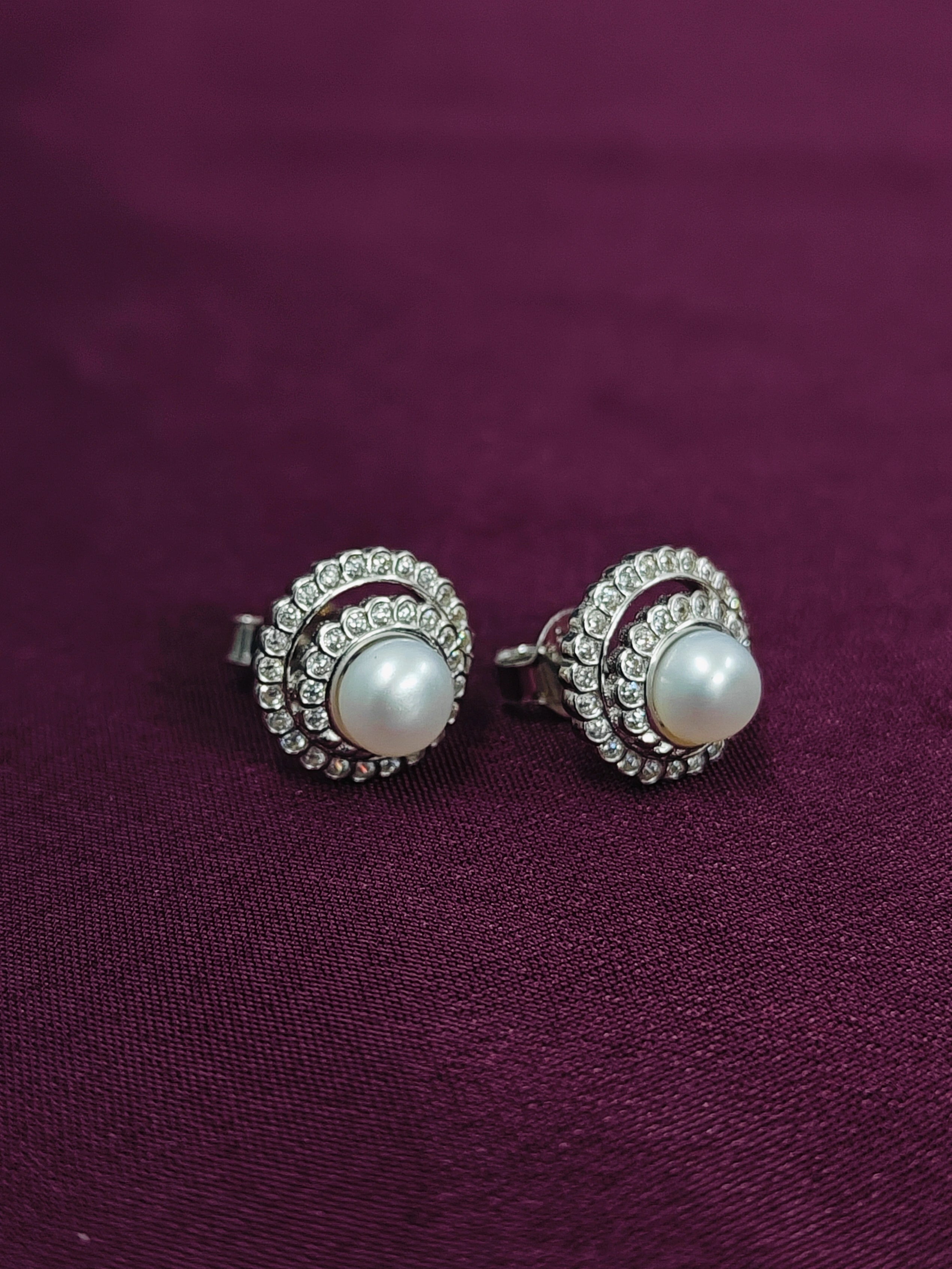Pair of pearl earrings with silver accents on a purple fabric background