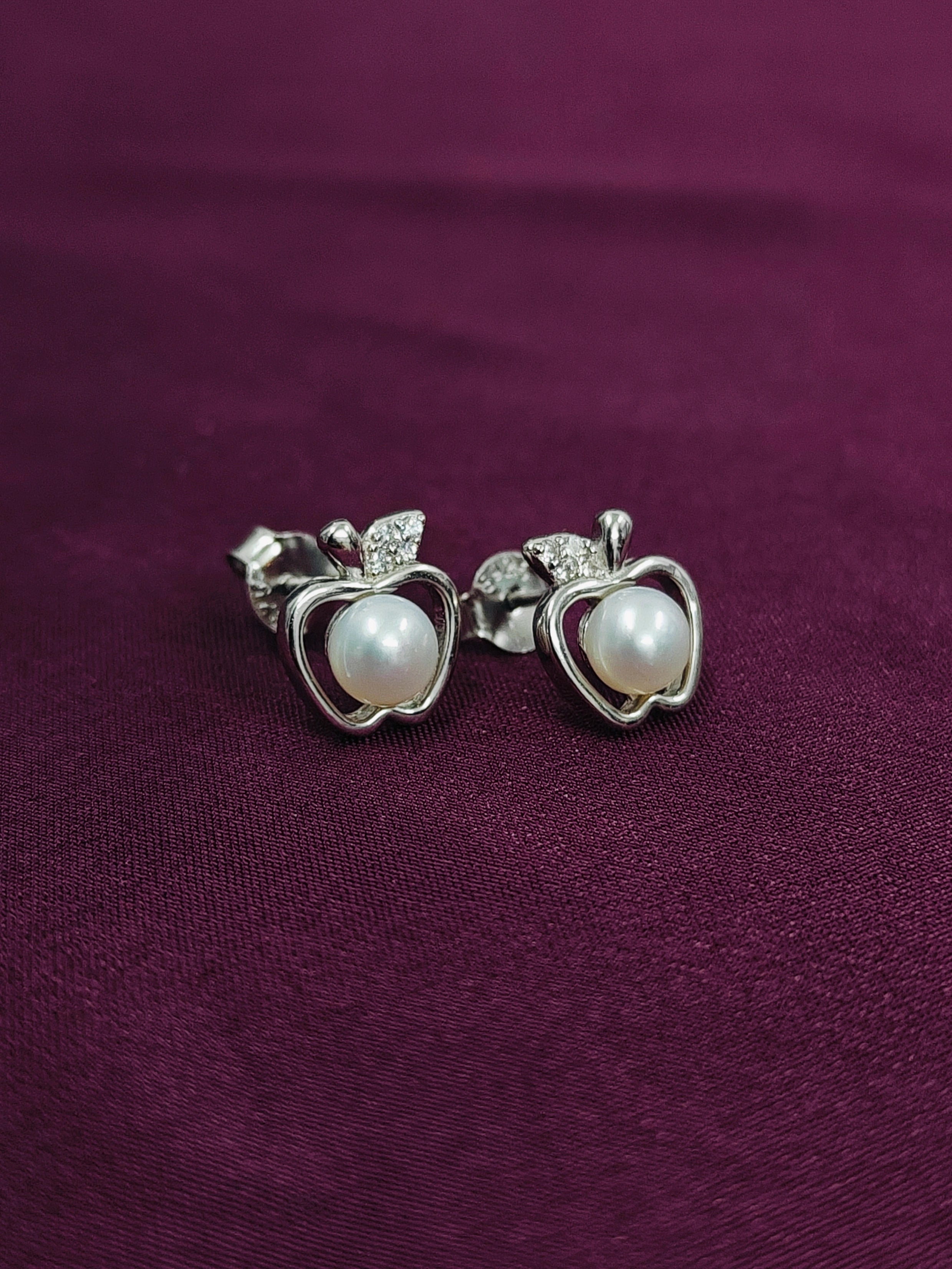 Silver apple-shaped earrings with pearls on a purple fabric background