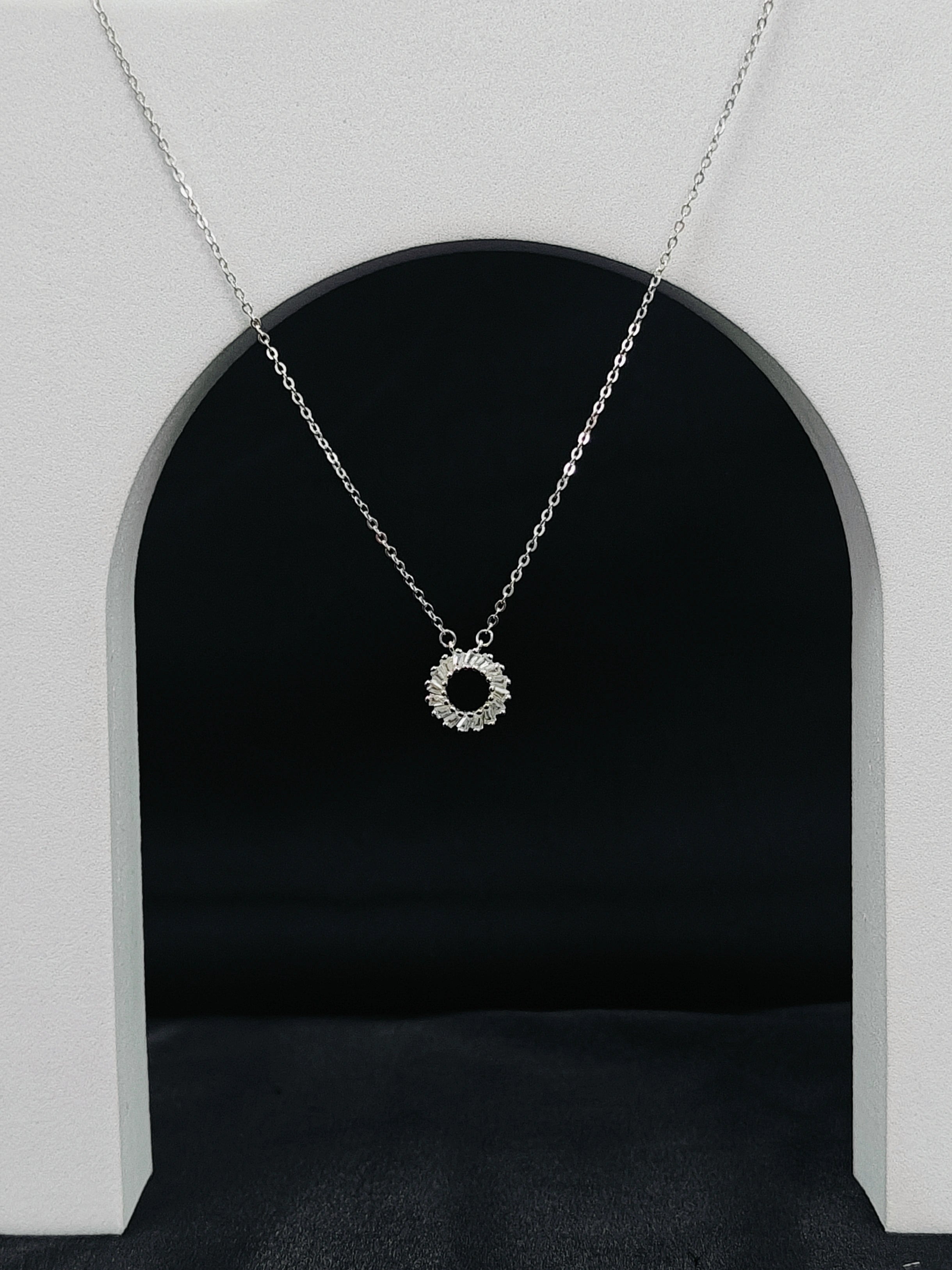 Silver necklace with a circular pendant hanging in front of a black archway.