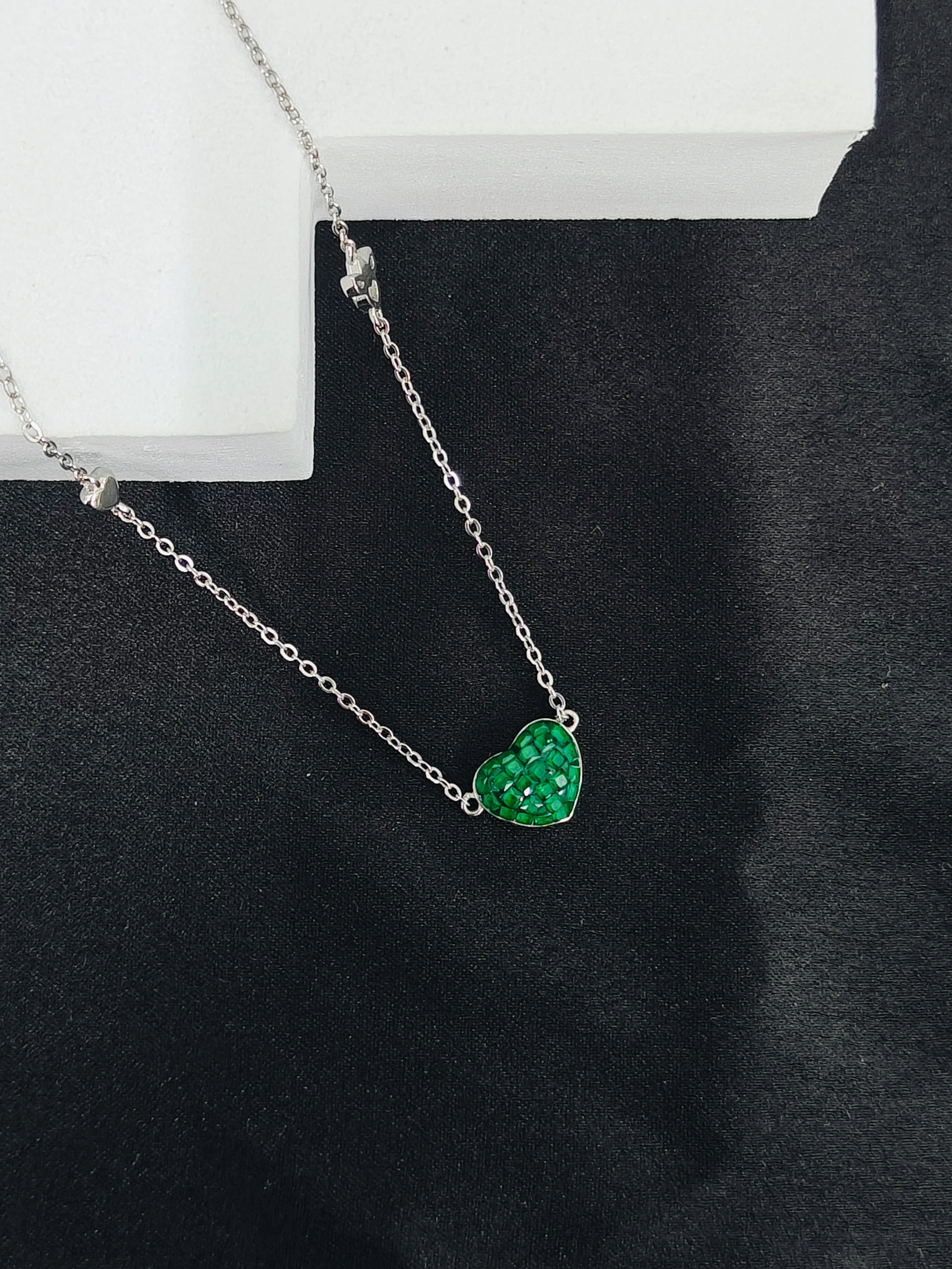 Silver necklace with a green heart-shaped pendant on a black background