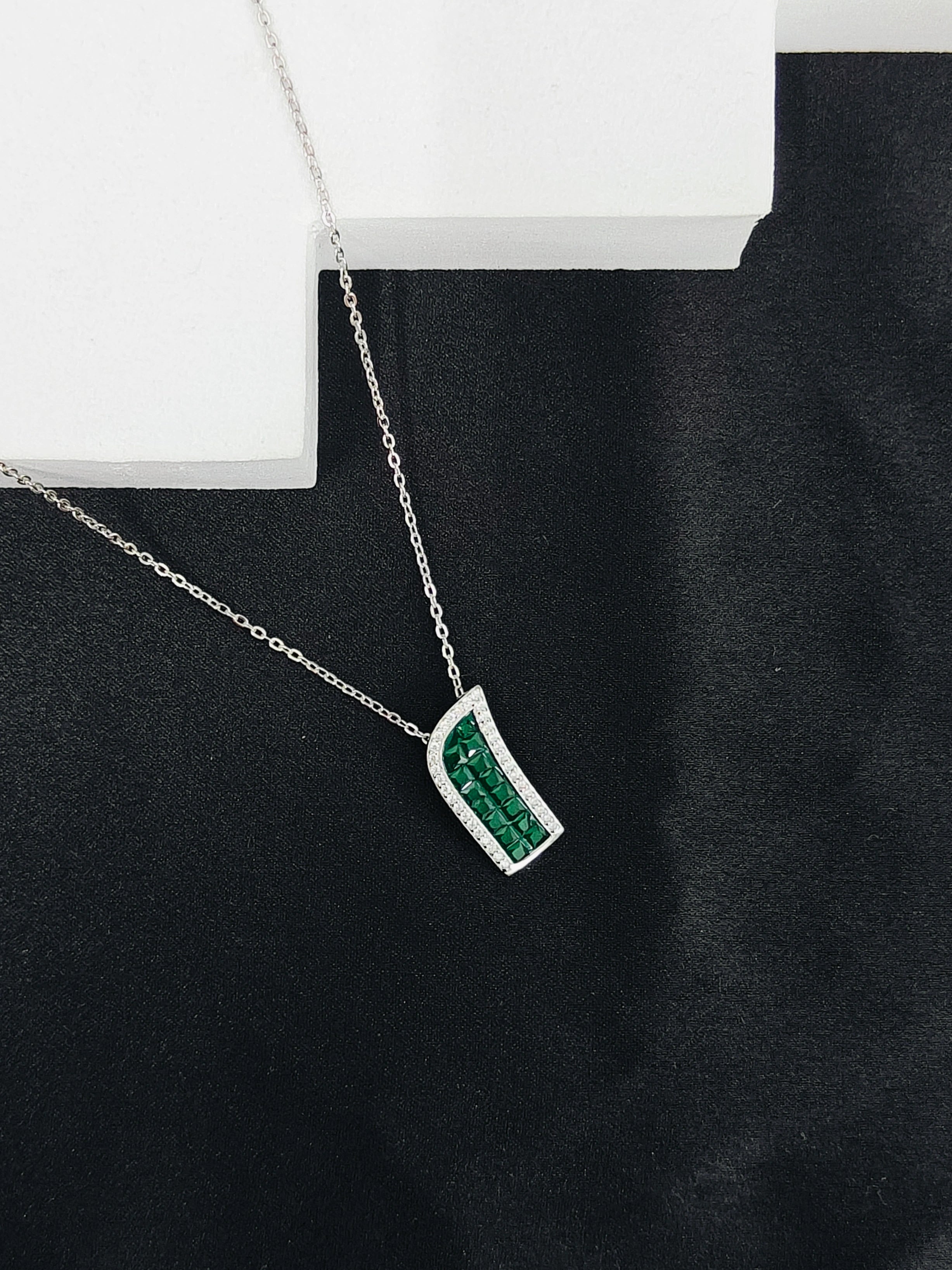 Silver necklace with a green gemstone pendant on a black surface