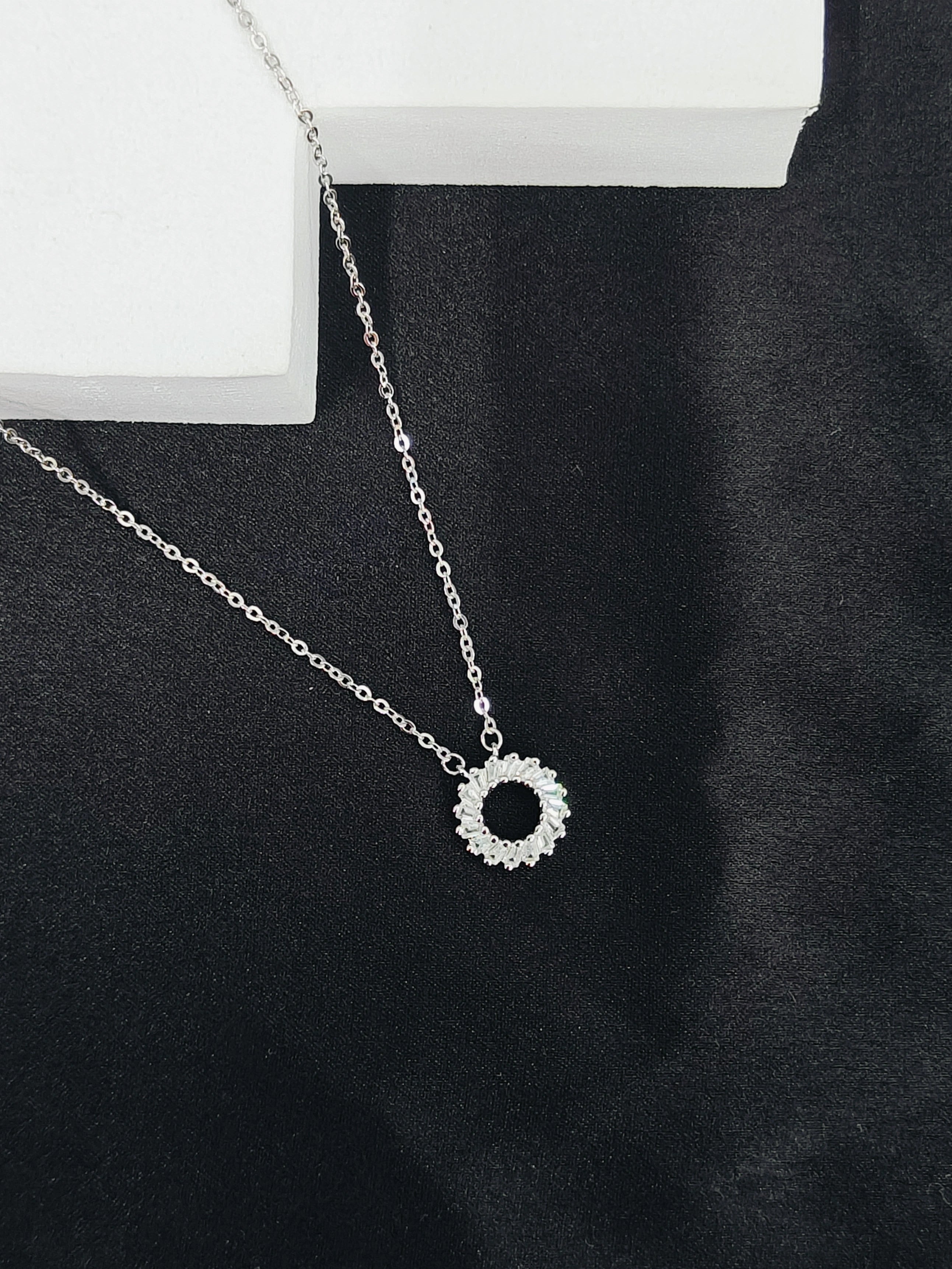 Silver necklace with a circular pendant on a black fabric background