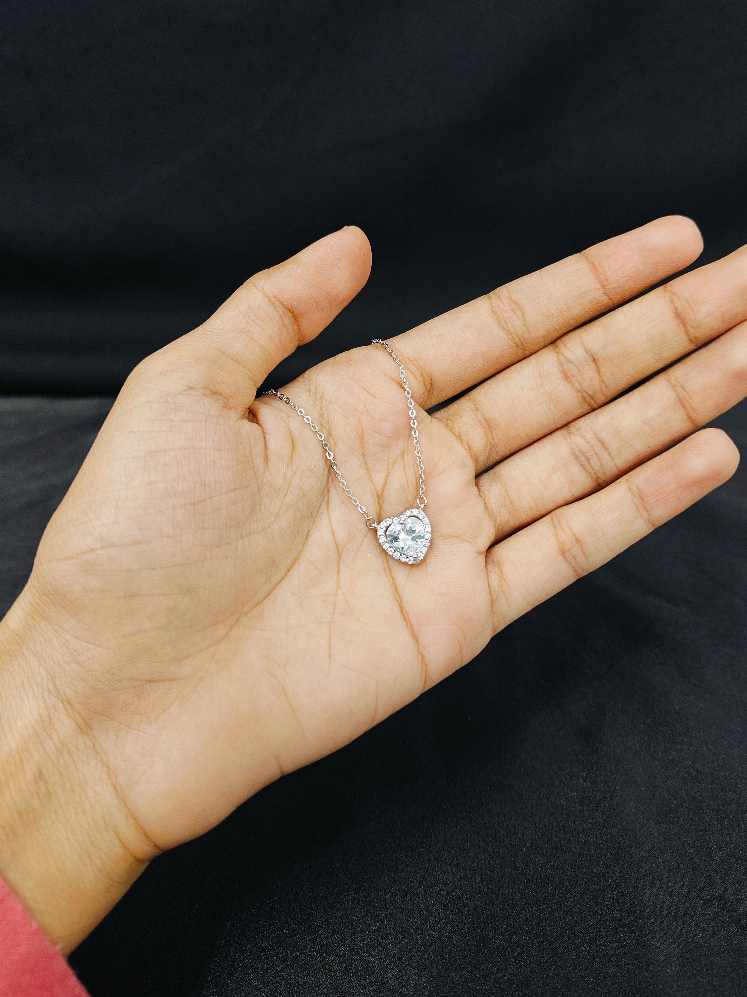 Heart-shaped diamond ring on a hand against a black background