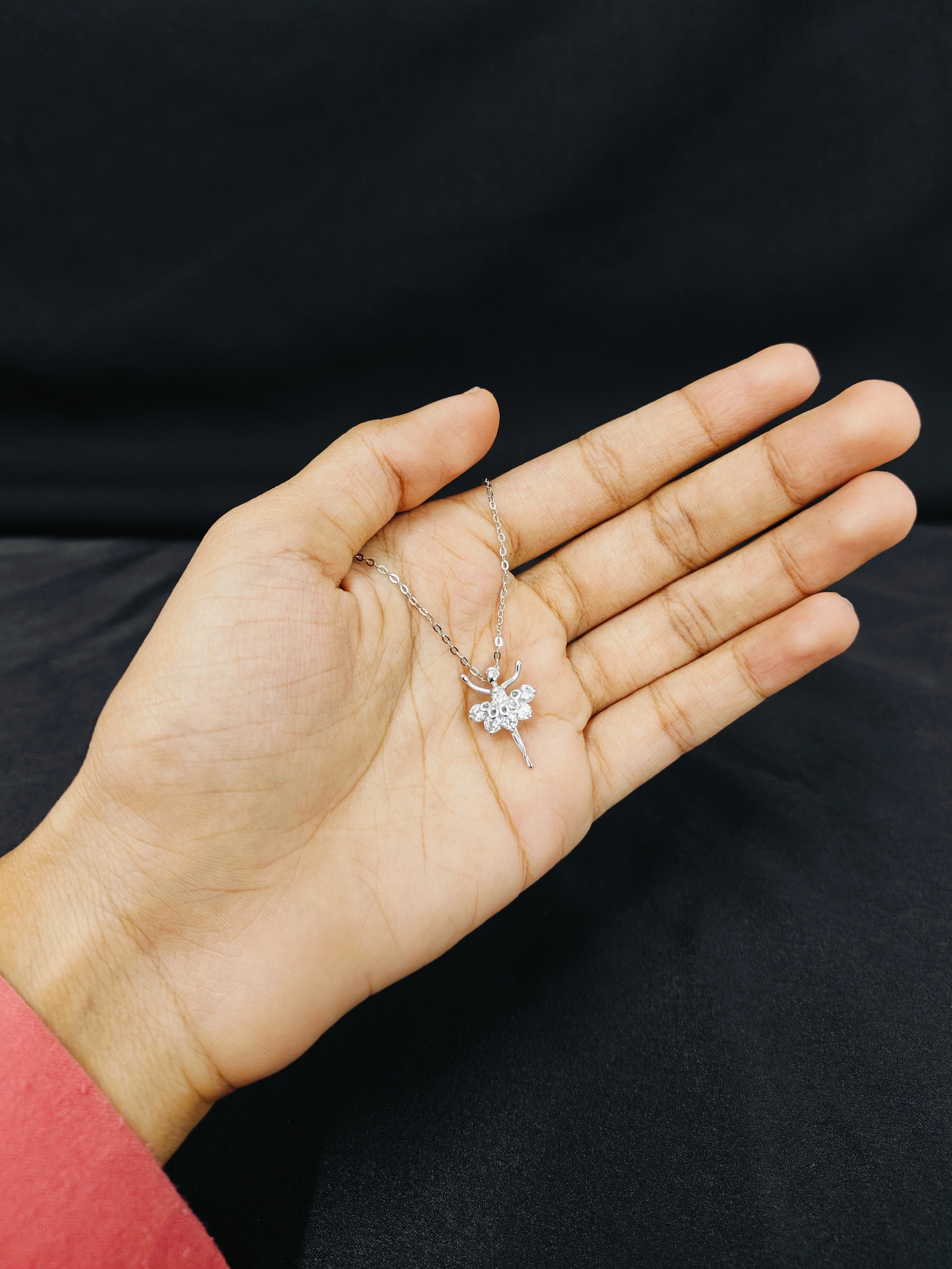 Hand holding a delicate necklace with a clear pendant against a black background