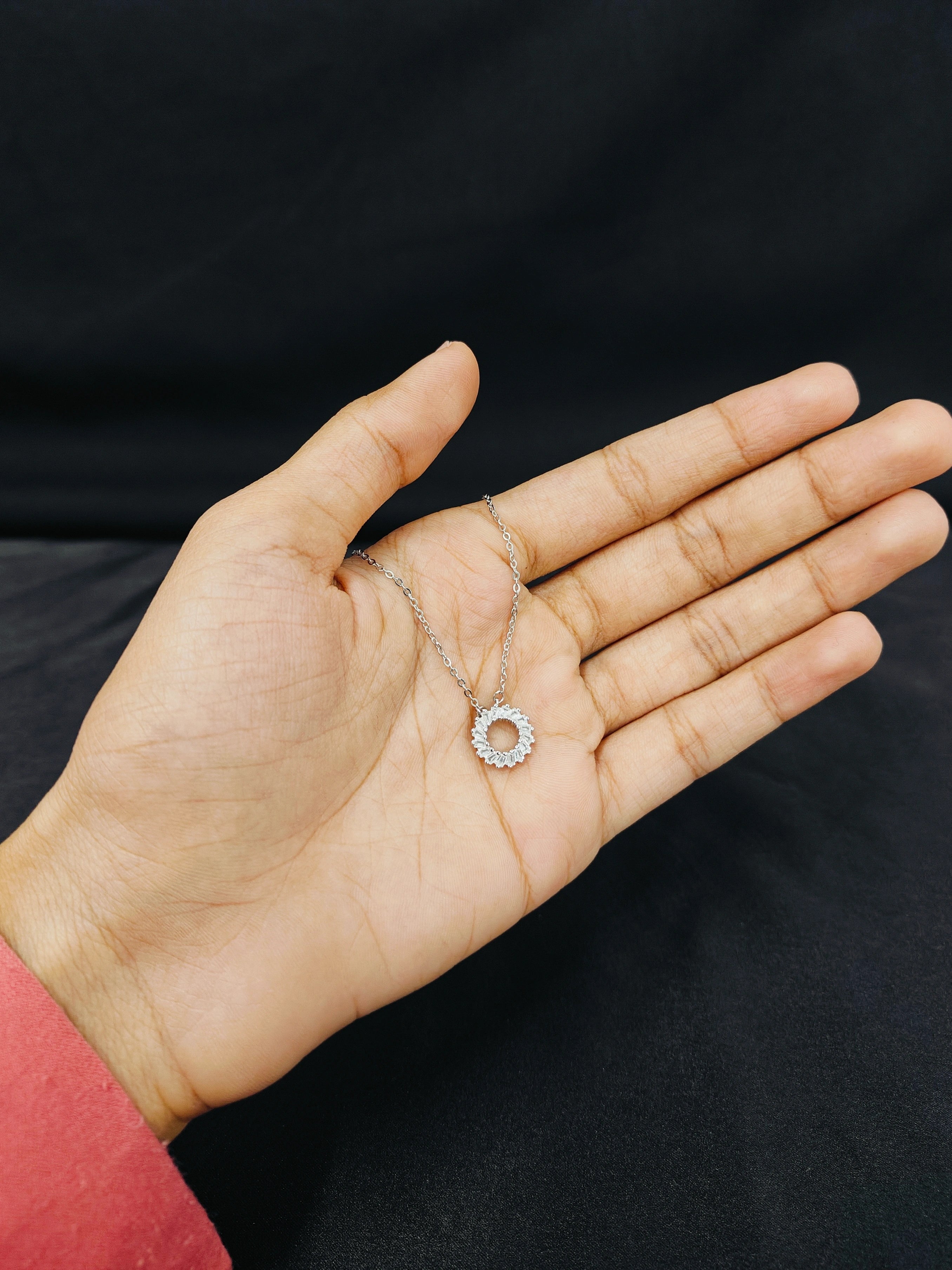 Hand holding a delicate silver necklace with a black background