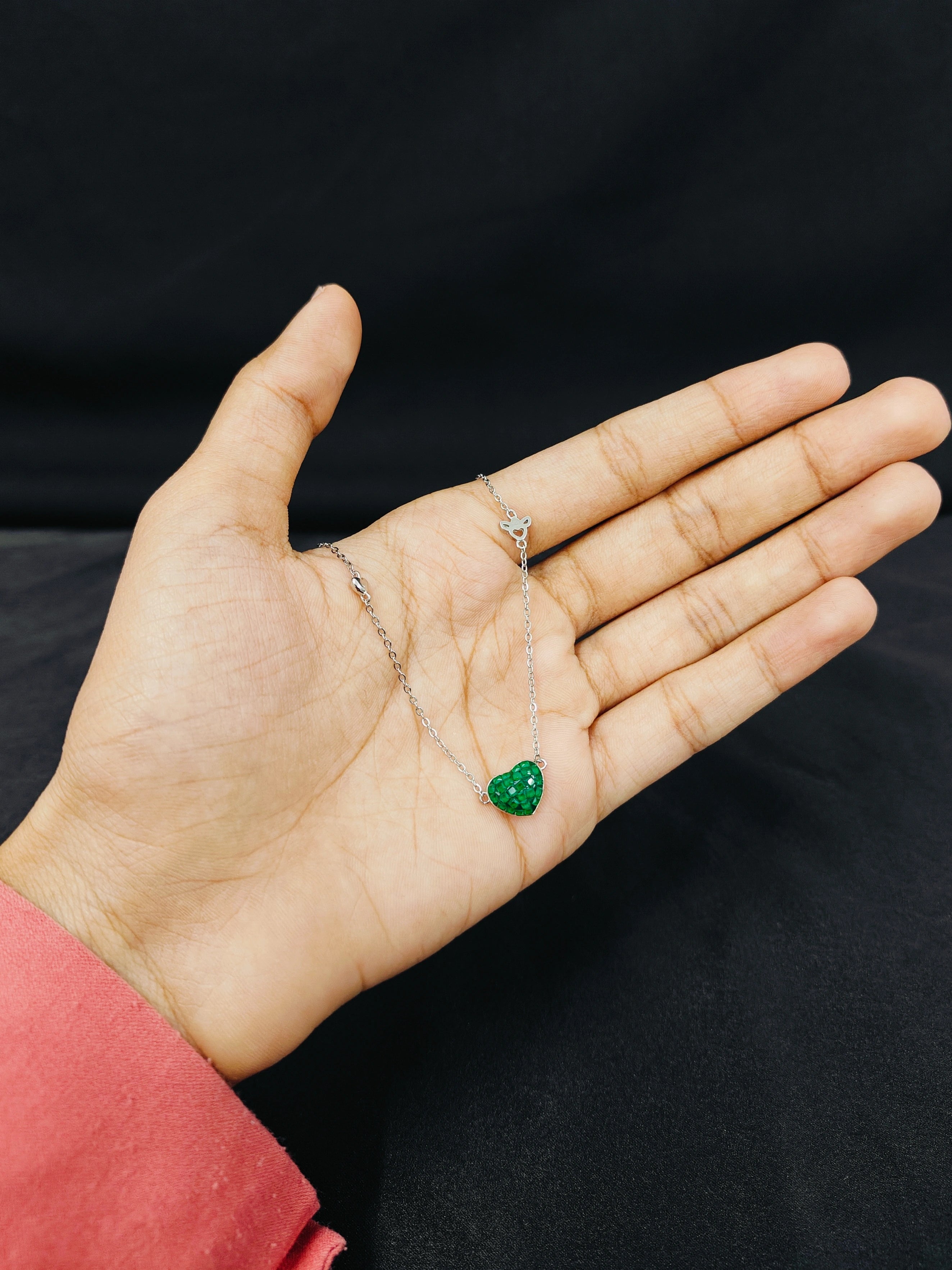 Hand holding a green gemstone and a diamond ring against a black background