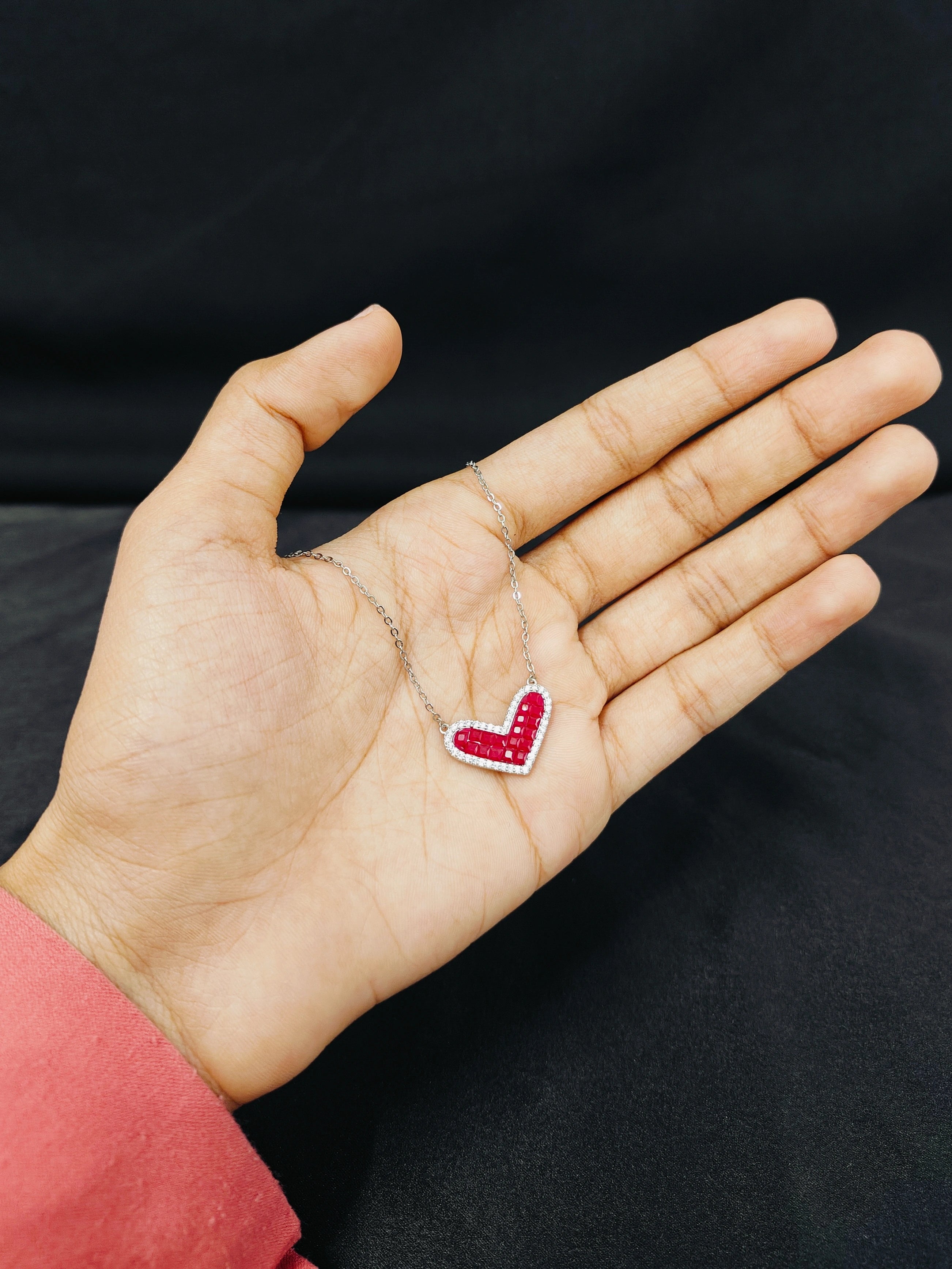 Hand holding a necklace with a red heart pendant against a black background
