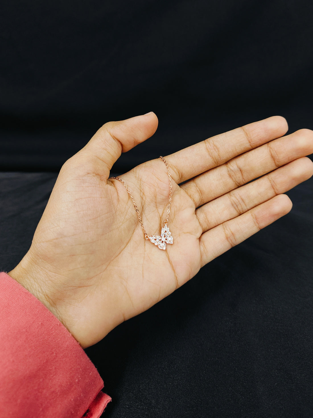 Hand holding a delicate necklace with a clear pendant against a black background