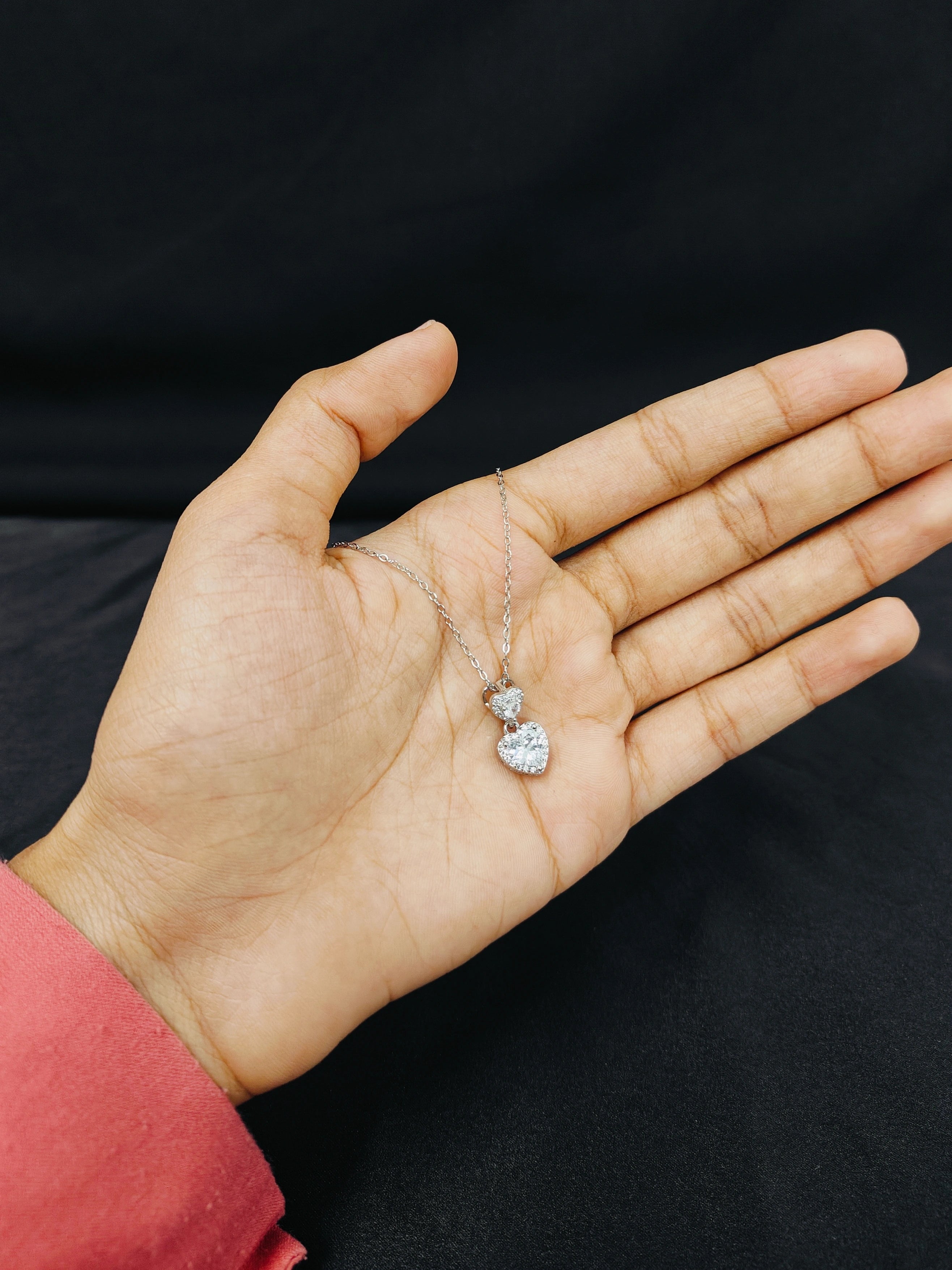 Hand holding a delicate necklace with a heart pendant against a black background