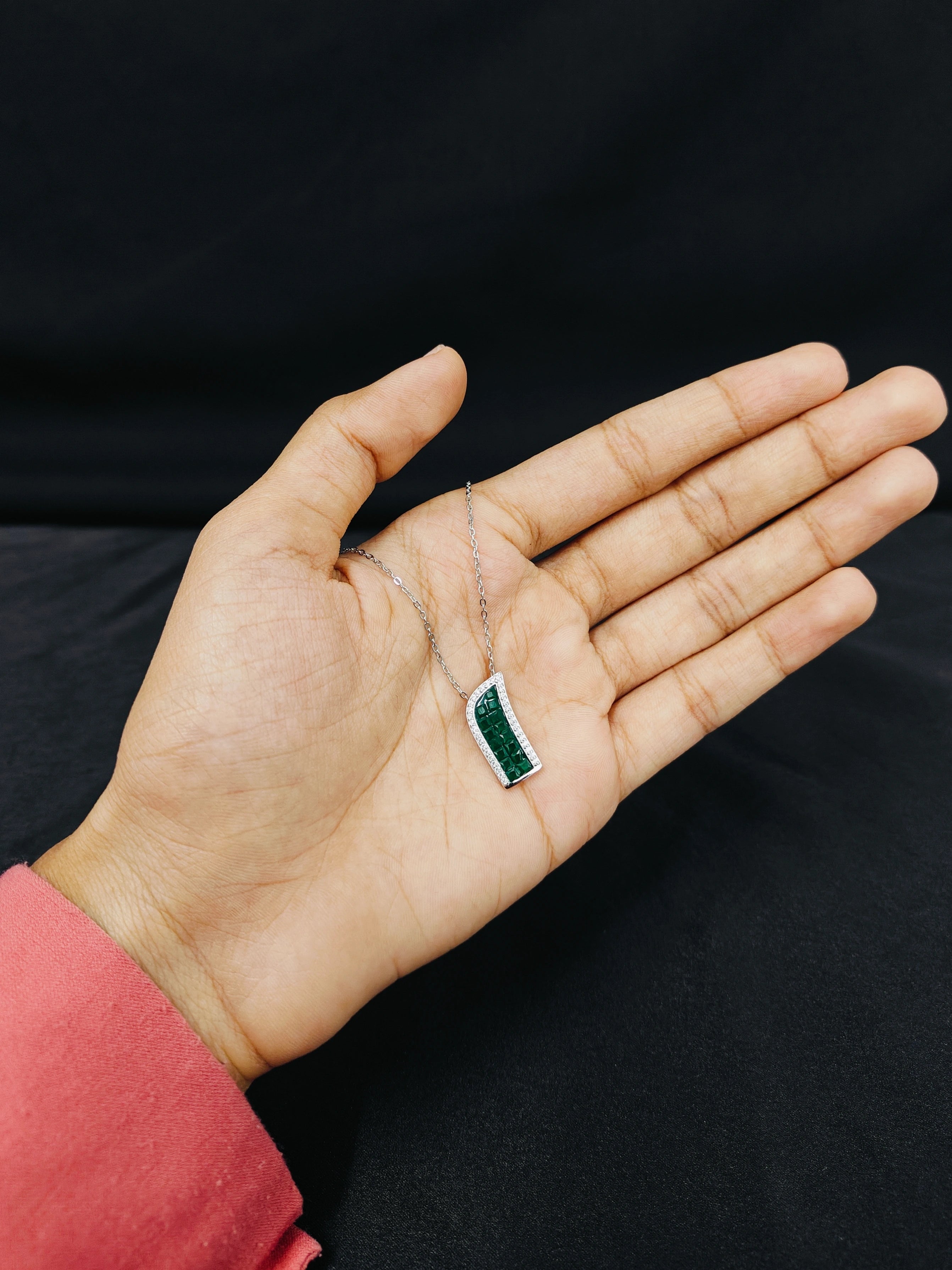 Hand holding a necklace with a green pendant against a black background