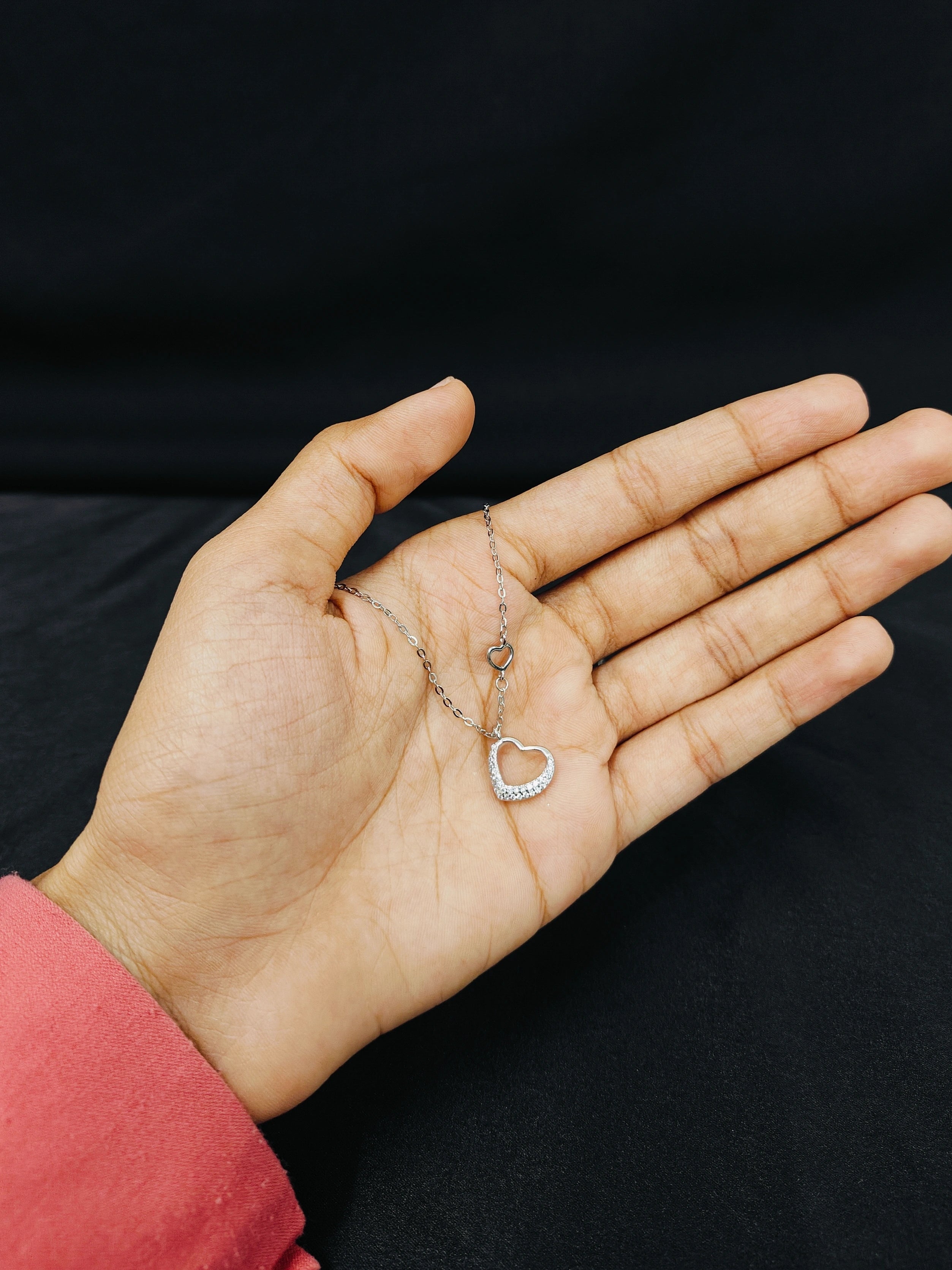 Hand holding a necklace with a heart pendant against a black background