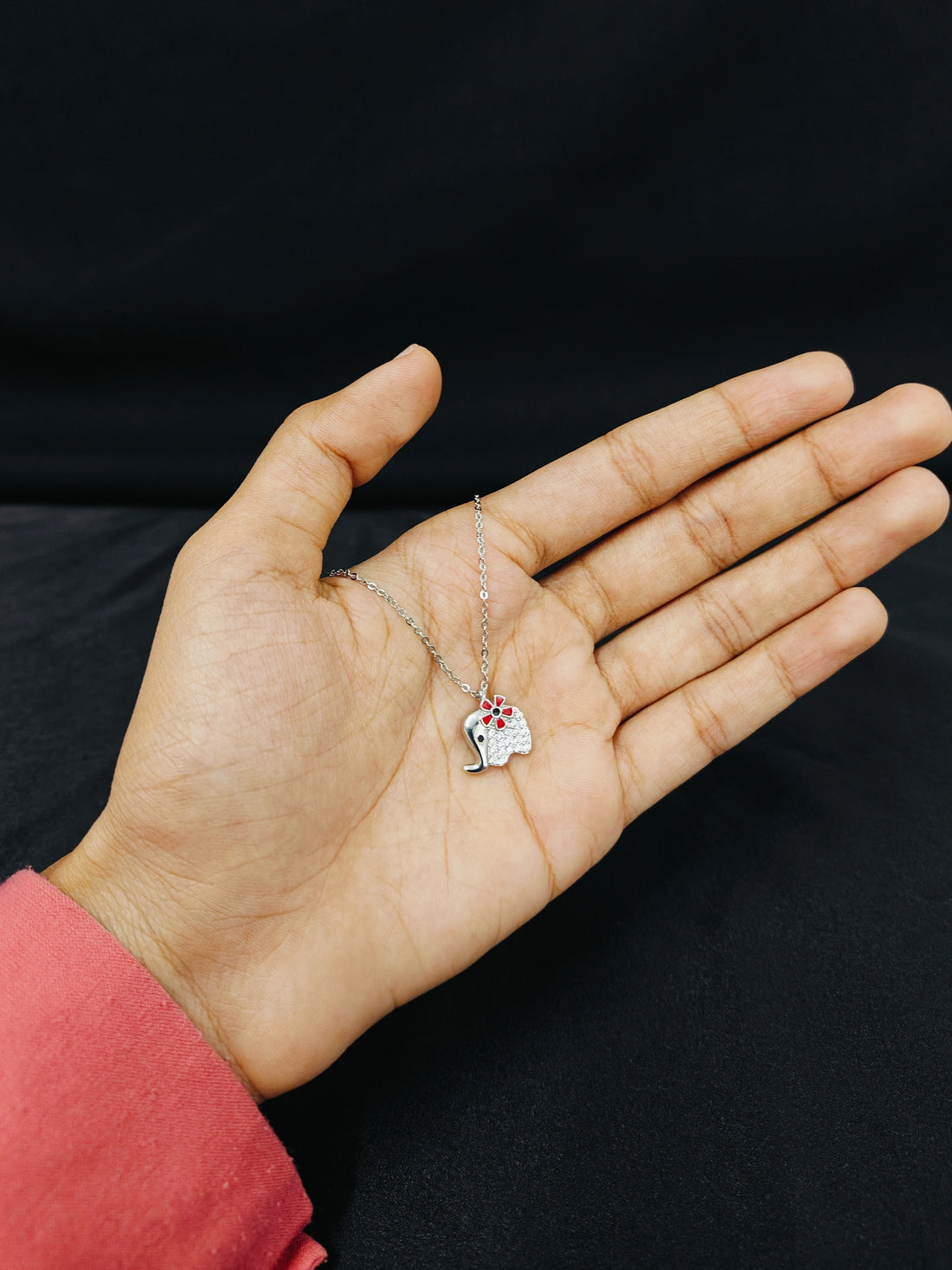 Hand holding a necklace with a small elephant pendant against a black background