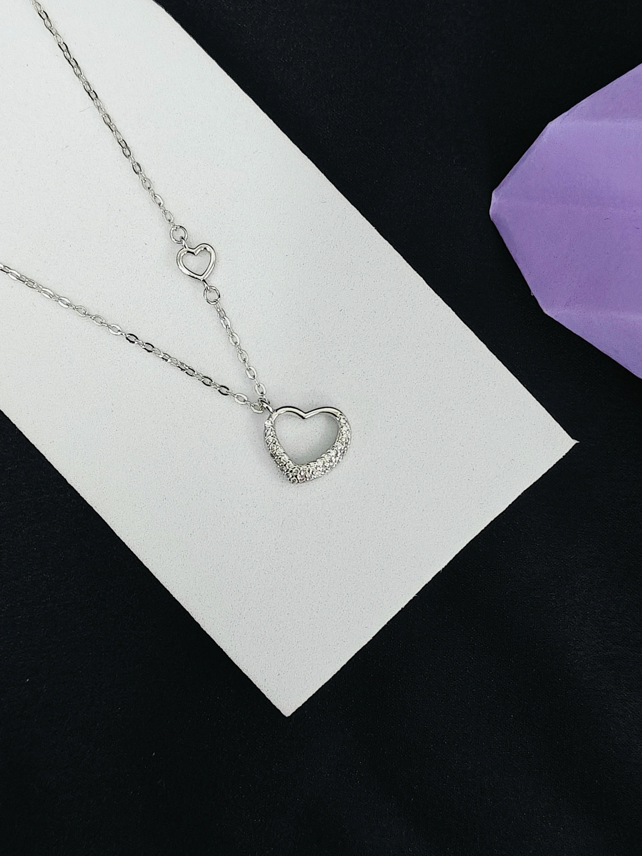 Silver heart-shaped necklace on a white card with a purple fabric background