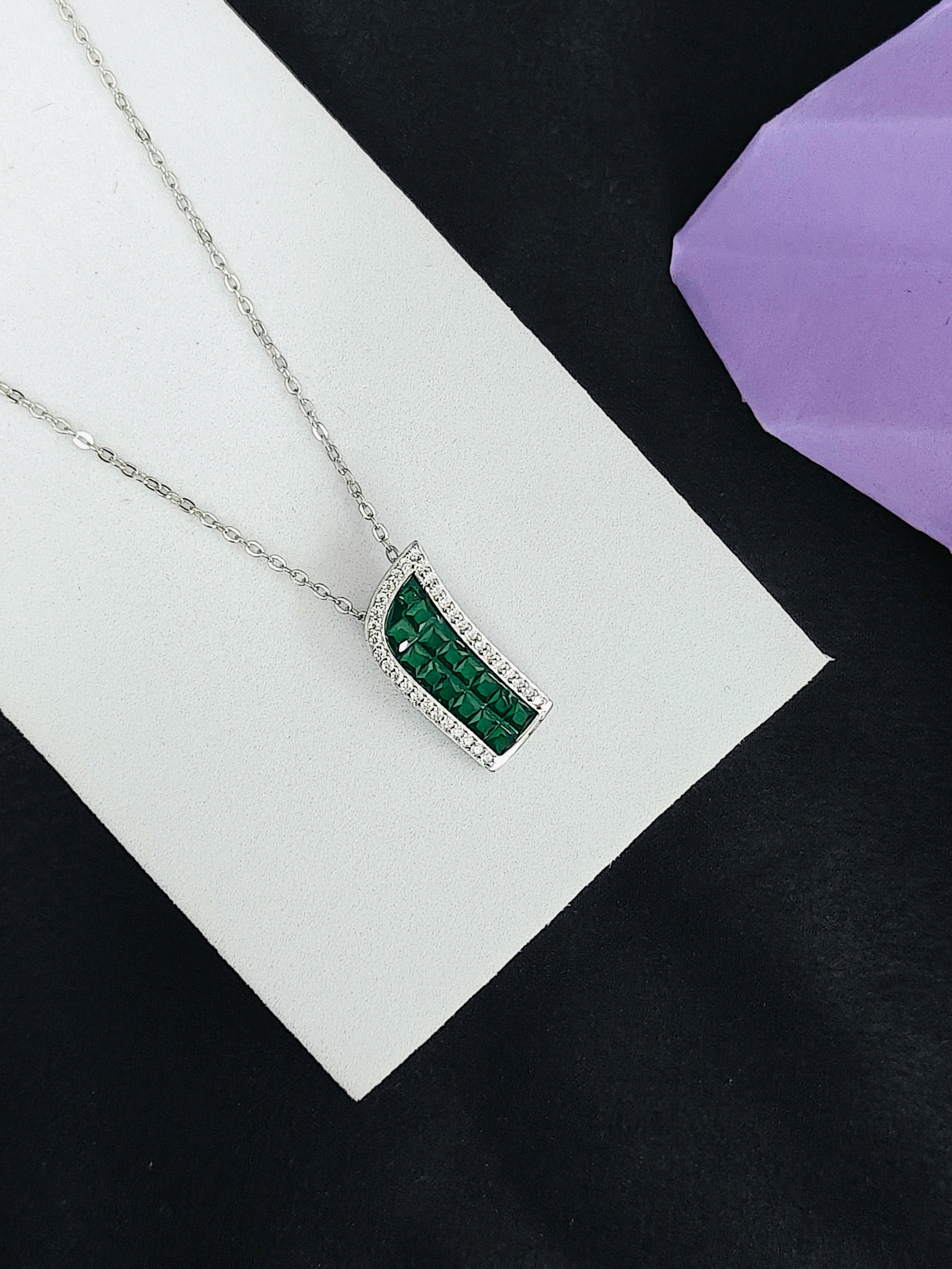 Silver necklace with a green pendant on a white card against a black background