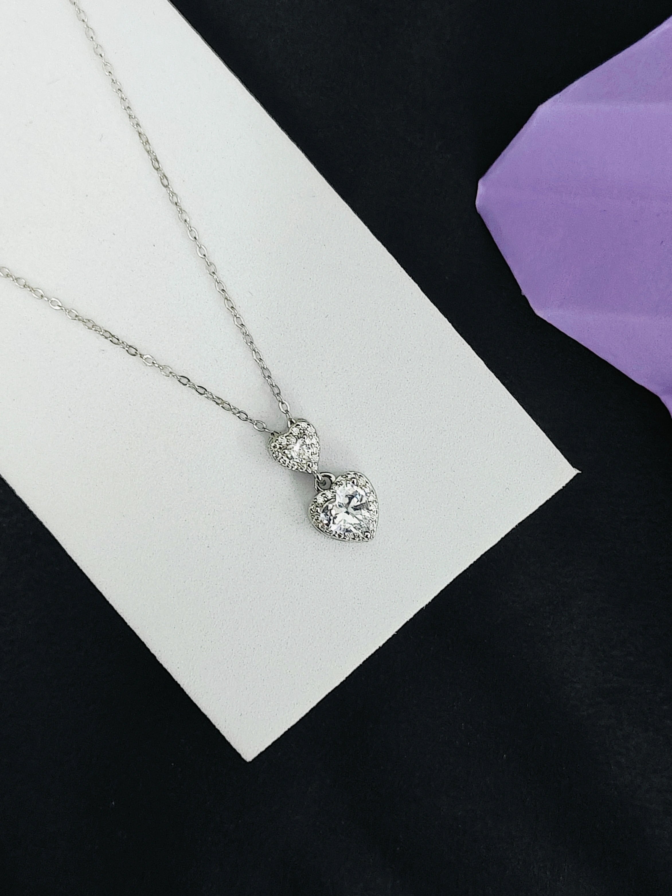 Silver necklace with a pendant on a white card against a black background