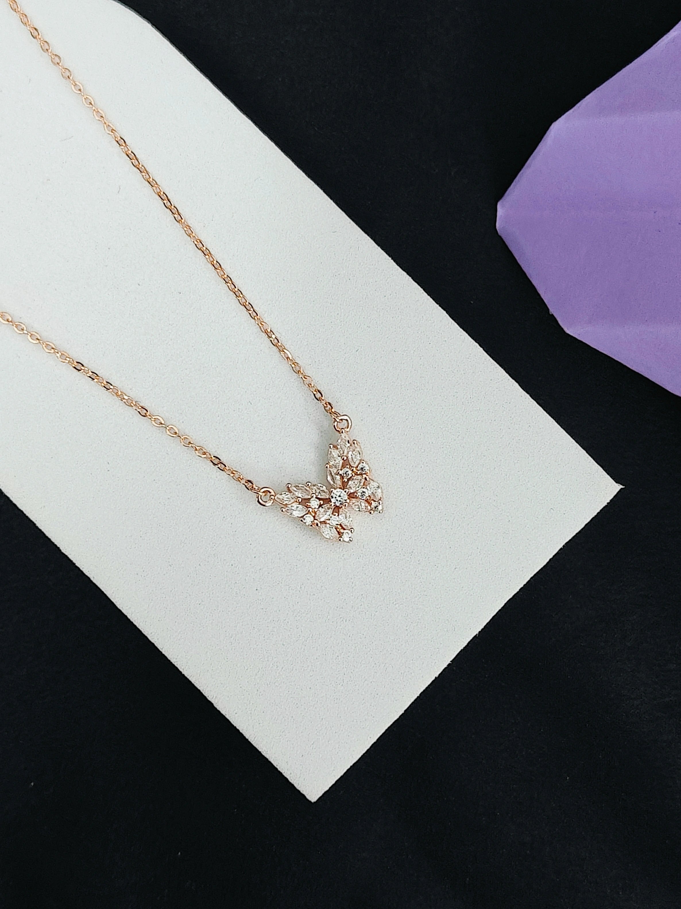 Rose gold necklace with floral design on a white card against a black background