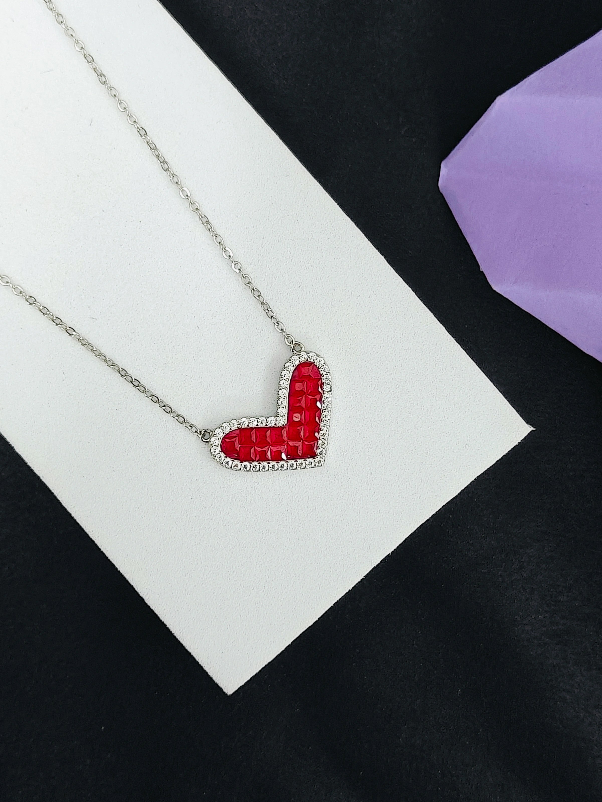 Necklace with a red heart-shaped pendant on a white card against a black background