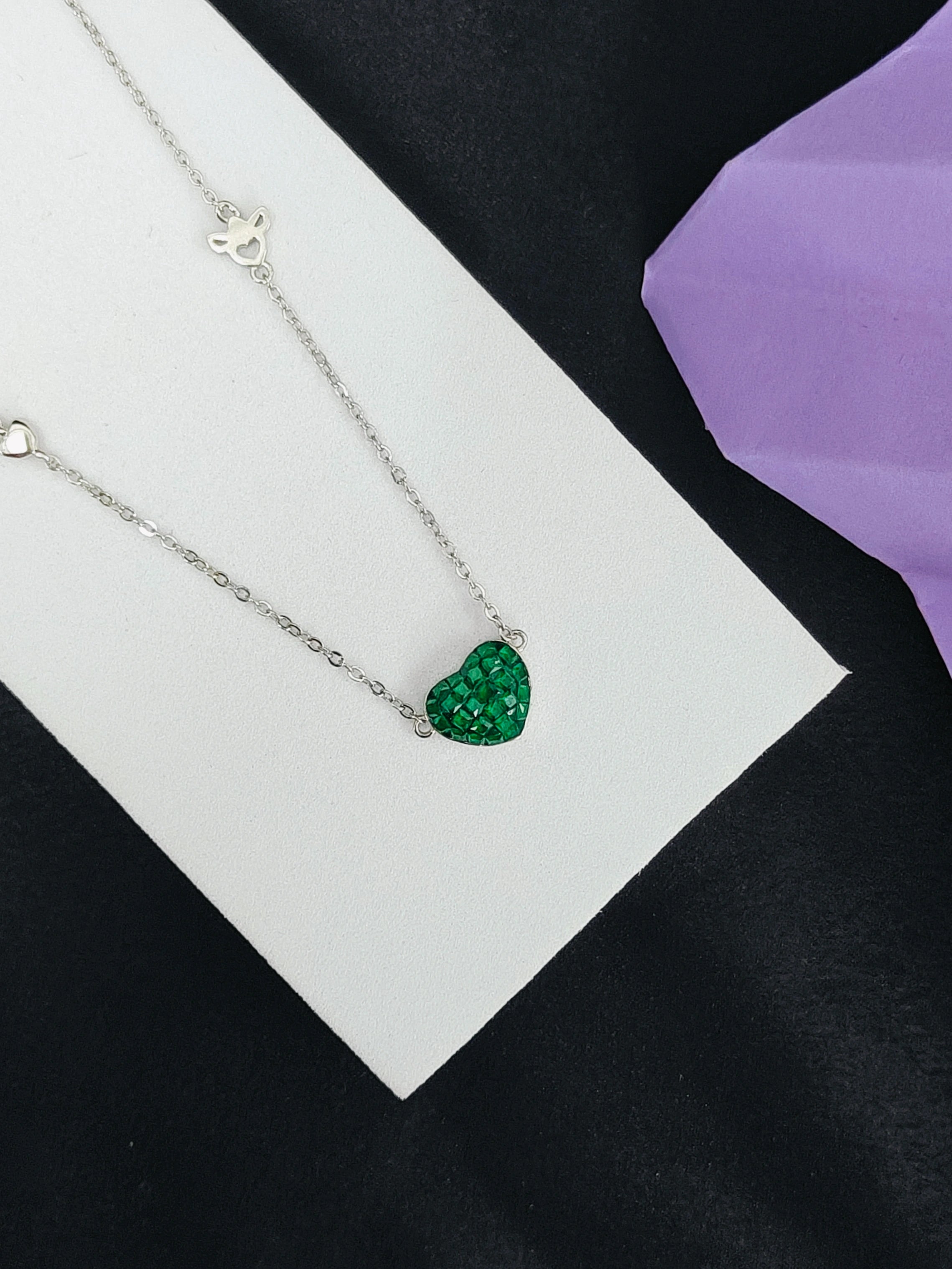 Necklace with a green heart-shaped pendant on a white card against a black background