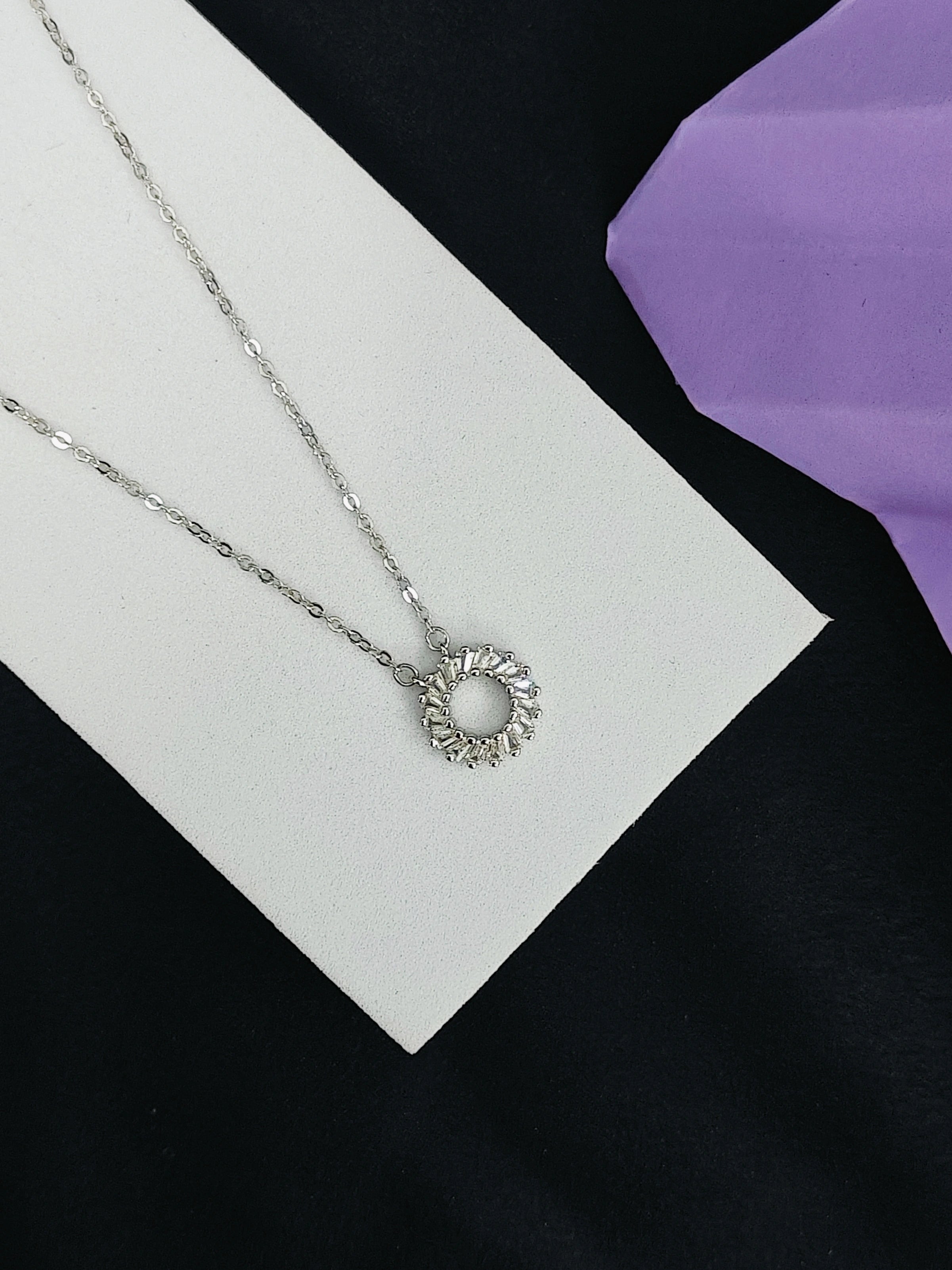 Silver necklace with a circular pendant on a white card with a purple fabric background