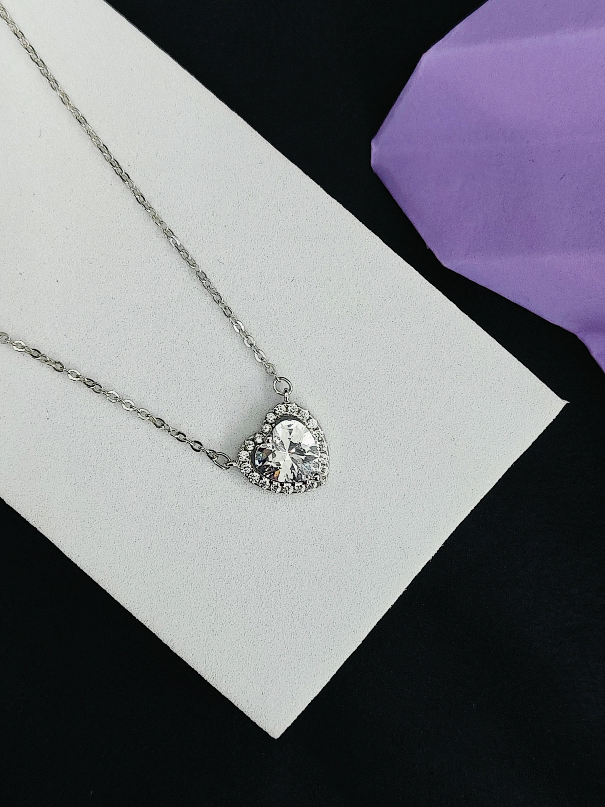 Silver necklace with a heart-shaped pendant on a white card with a purple fabric background