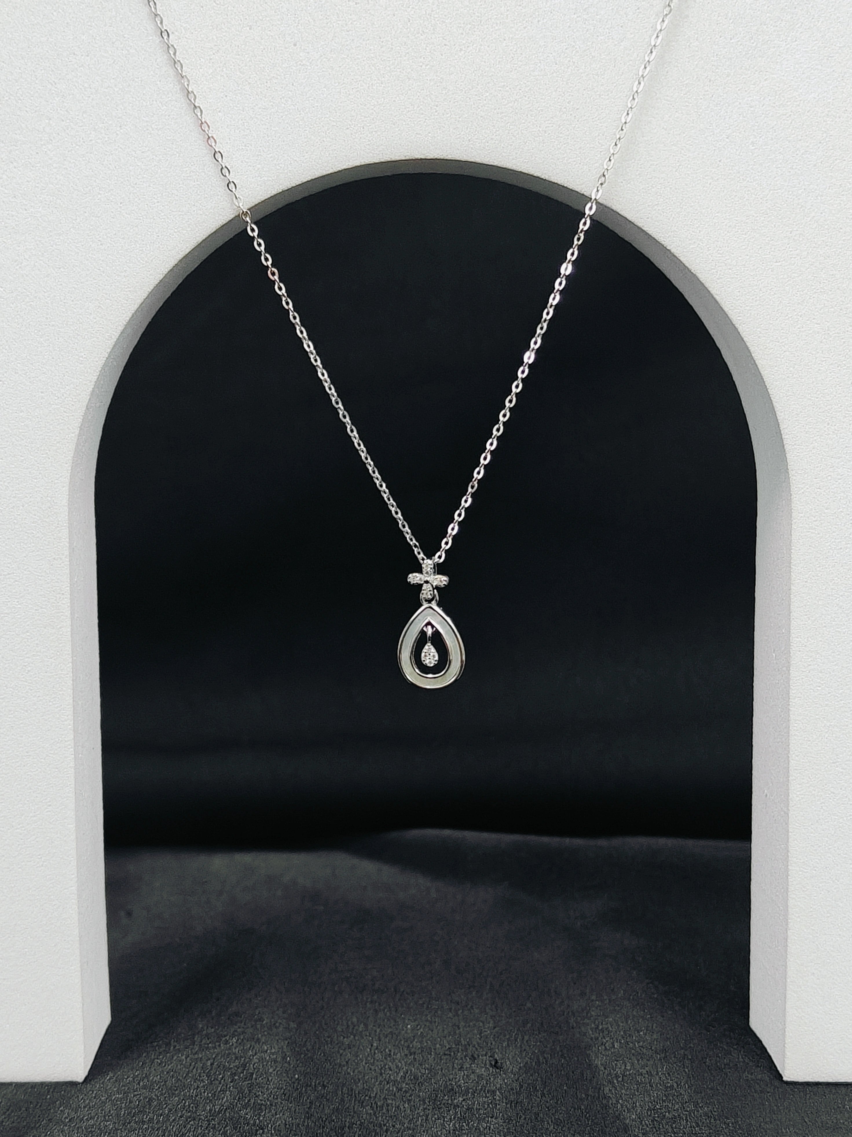Silver necklace with a teardrop pendant hanging in front of a black archway.