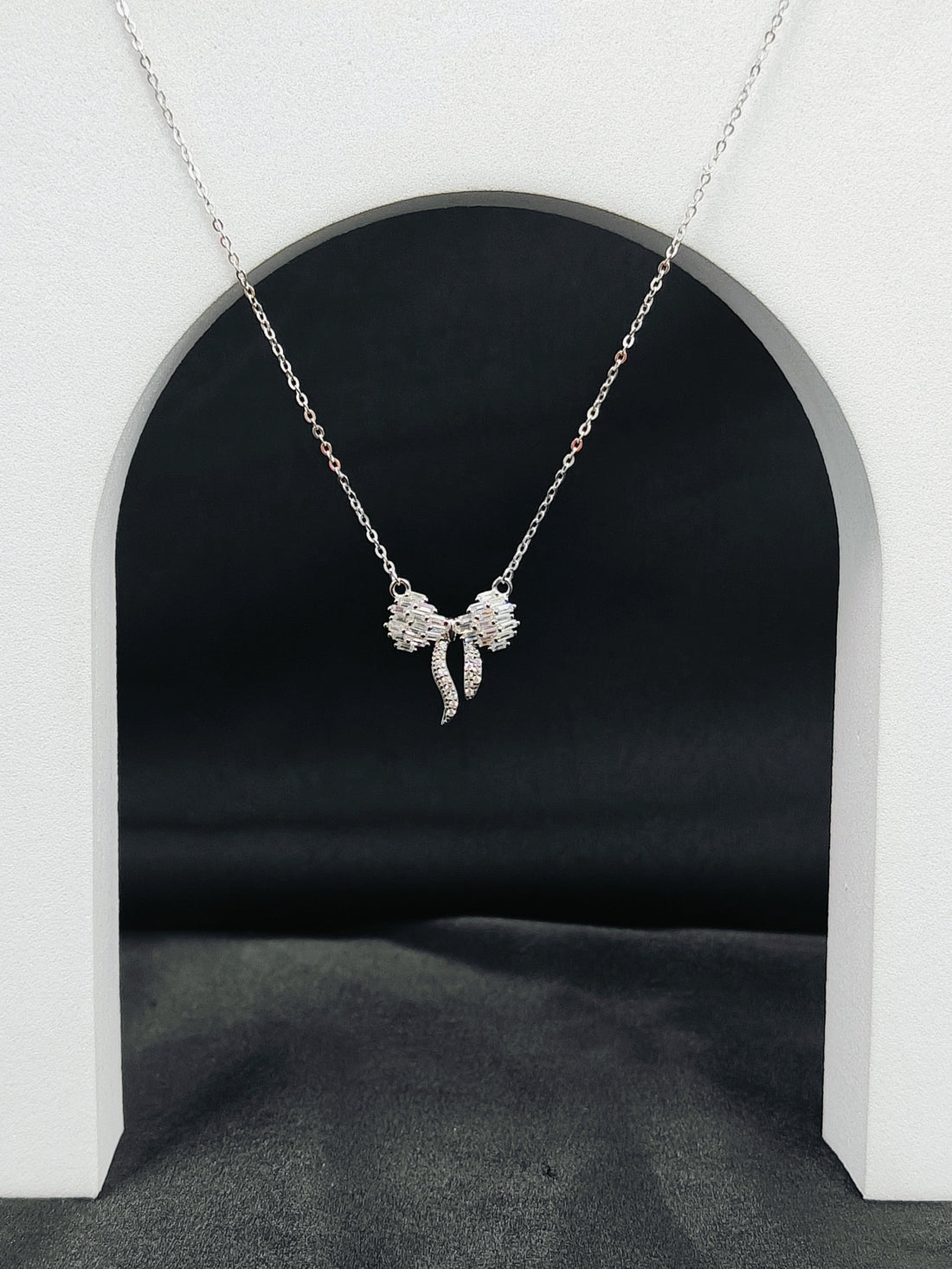 Silver bow-shaped pendant necklace on a white archway background
