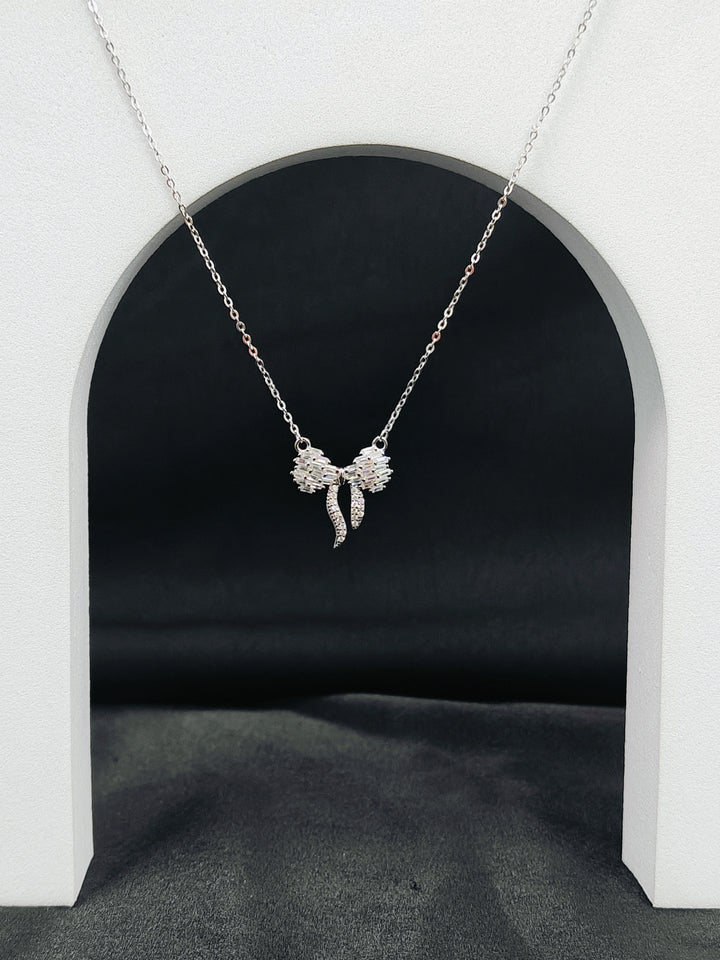 Silver bow-shaped pendant necklace on a white archway background