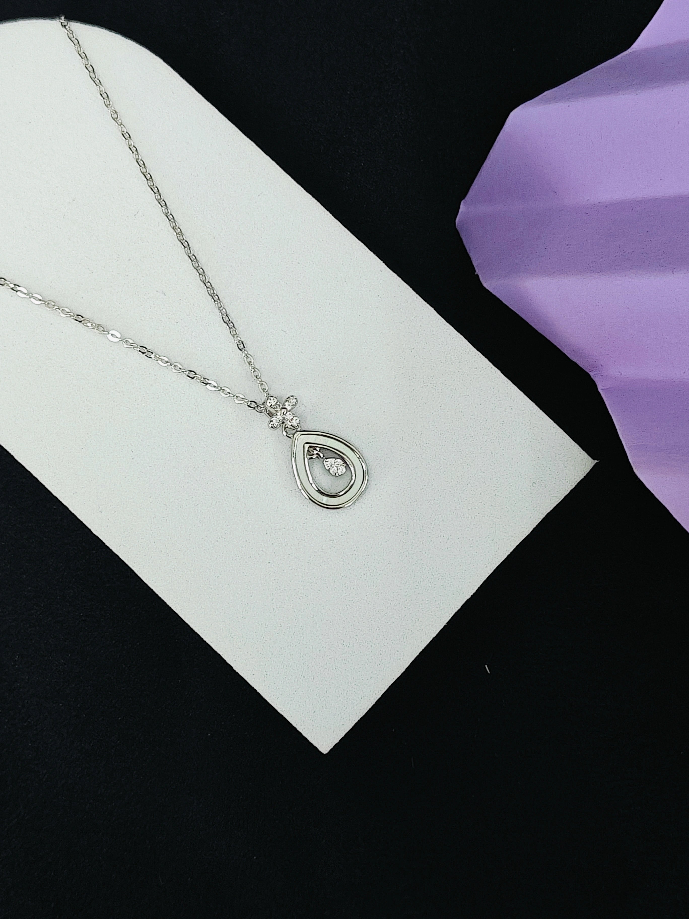 Silver necklace with a teardrop pendant on a white card against a black background
