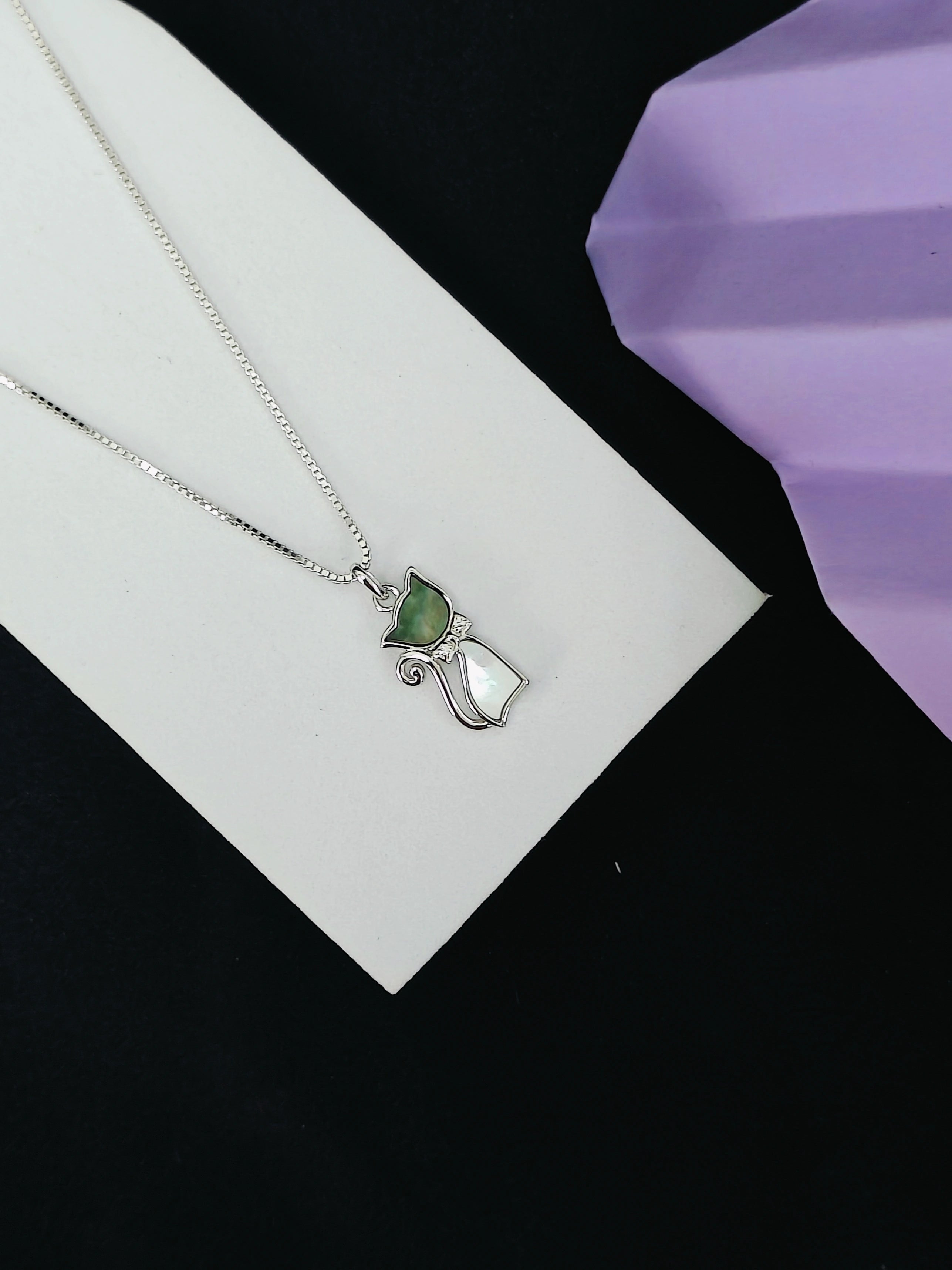 Silver necklace with a green pendant on a white card against a black background