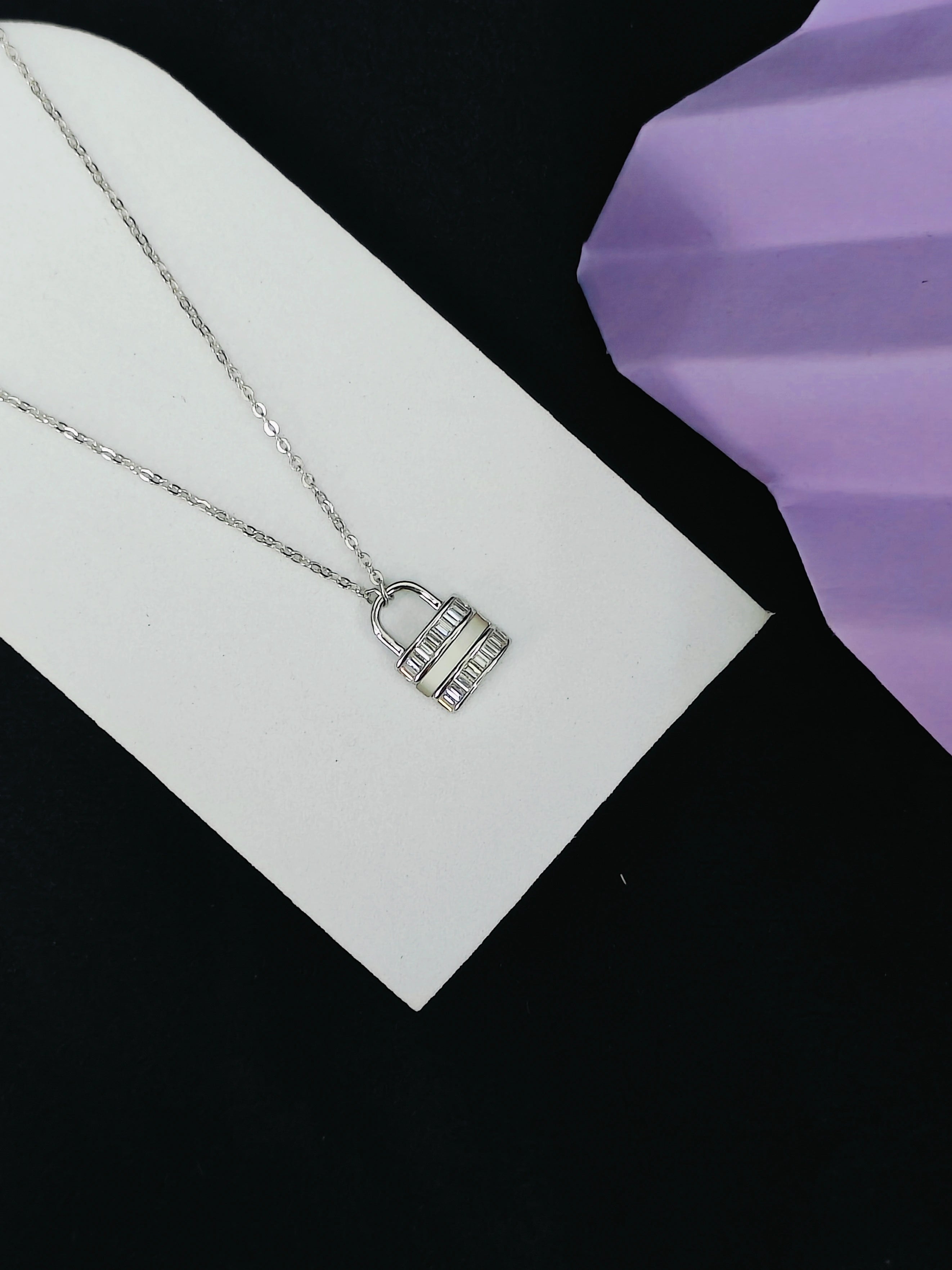 Silver necklace with a pendant on a white card against a black background