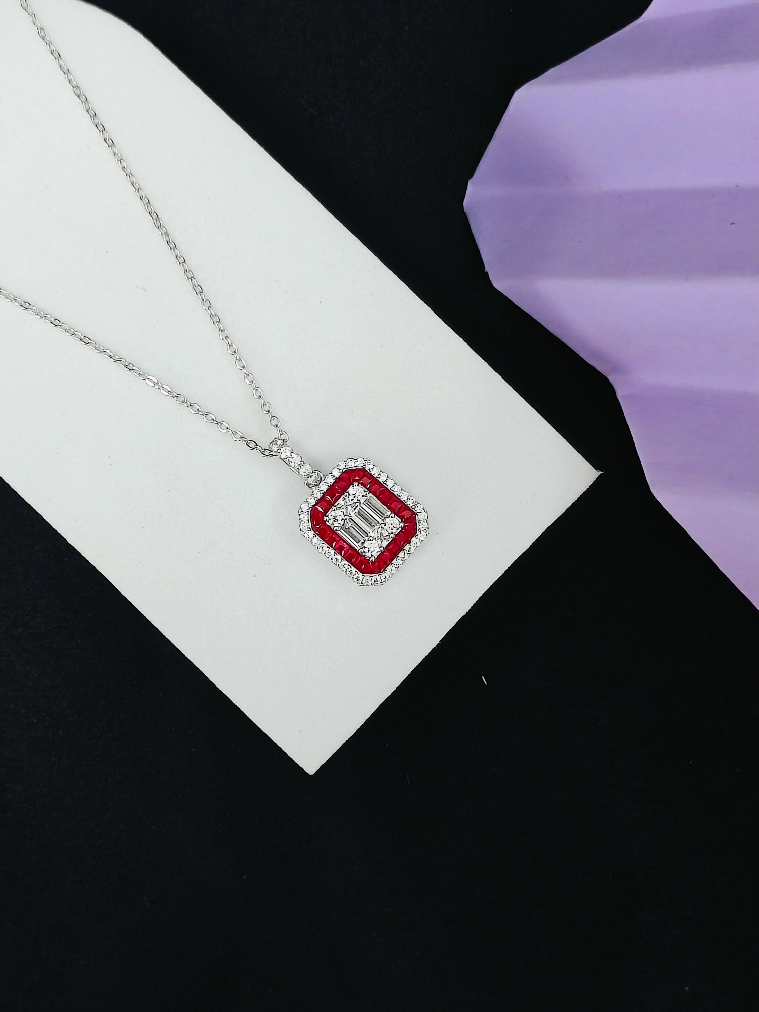 Necklace with a red gemstone pendant on a white card against a black background