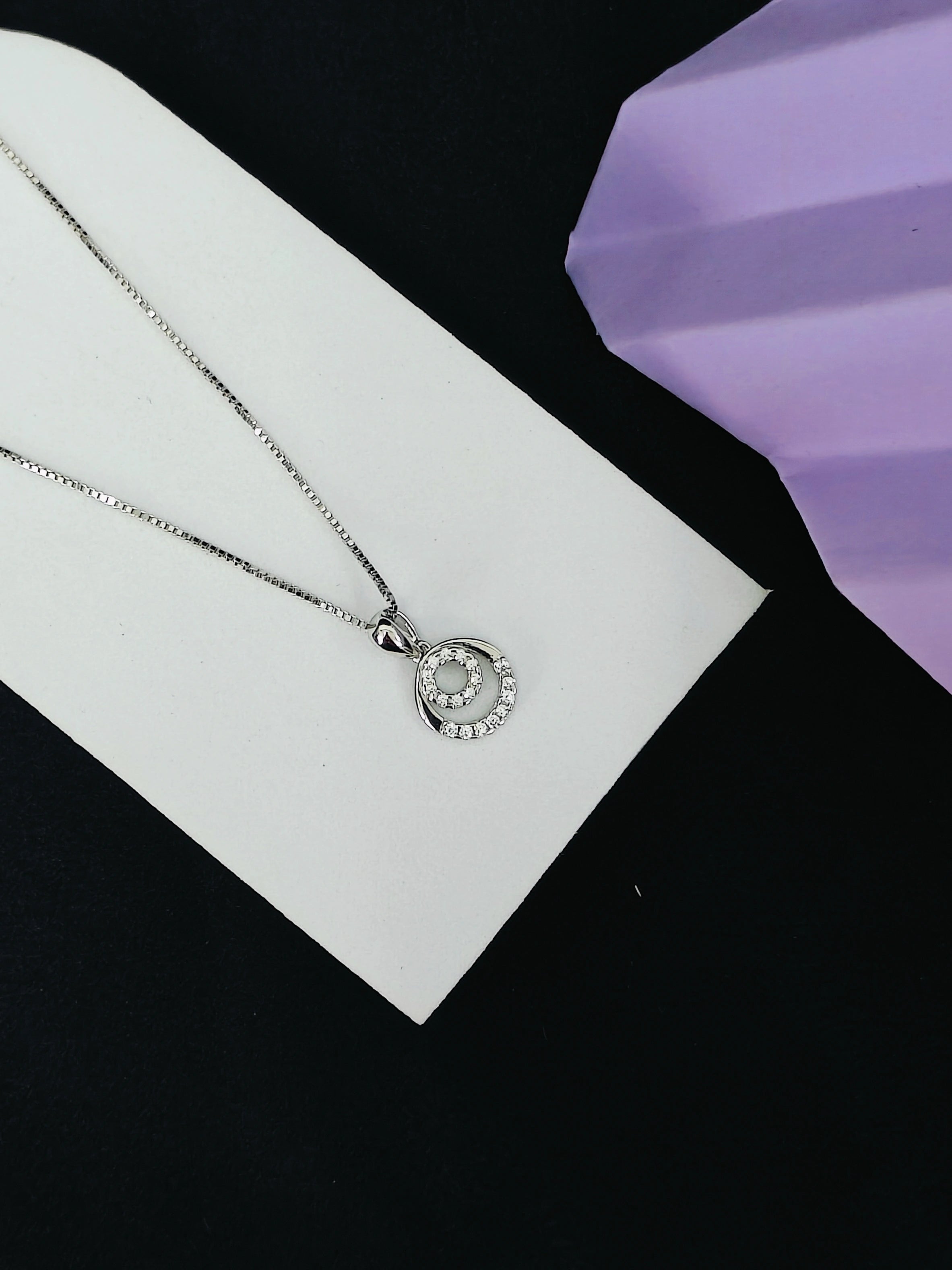 Silver necklace with a circular pendant on a white card against a black background