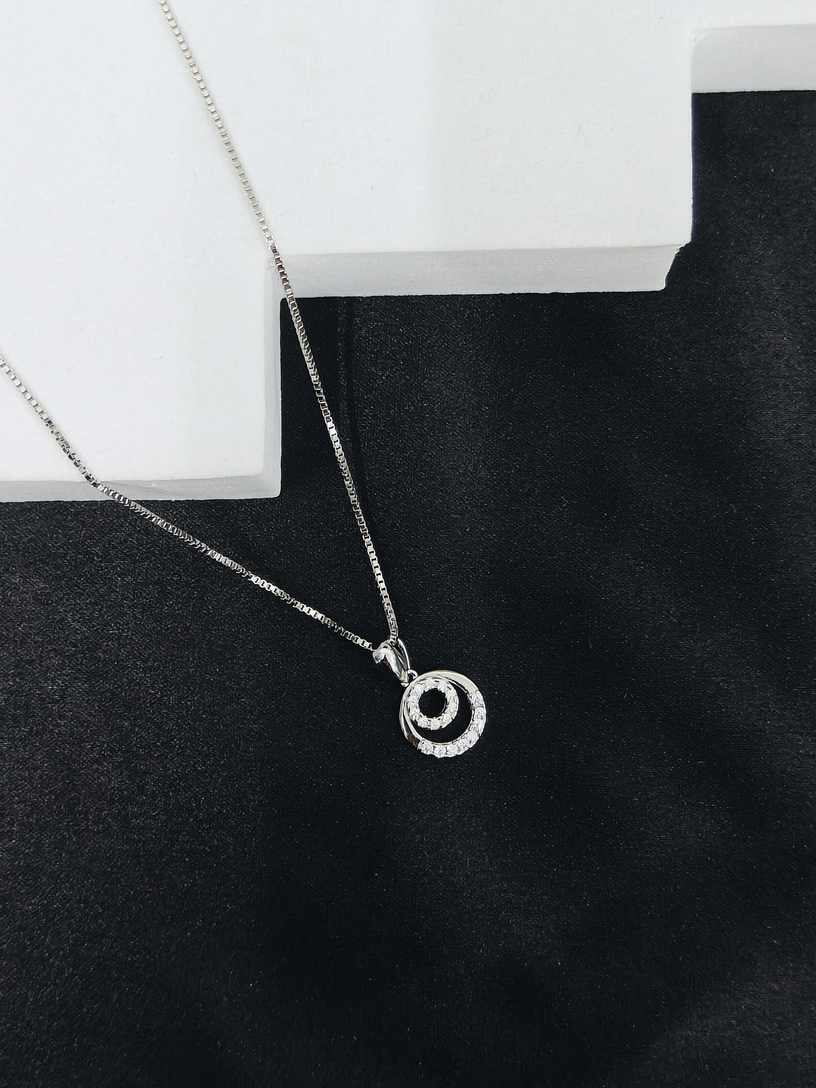 Silver necklace with a circular pendant on a black surface
