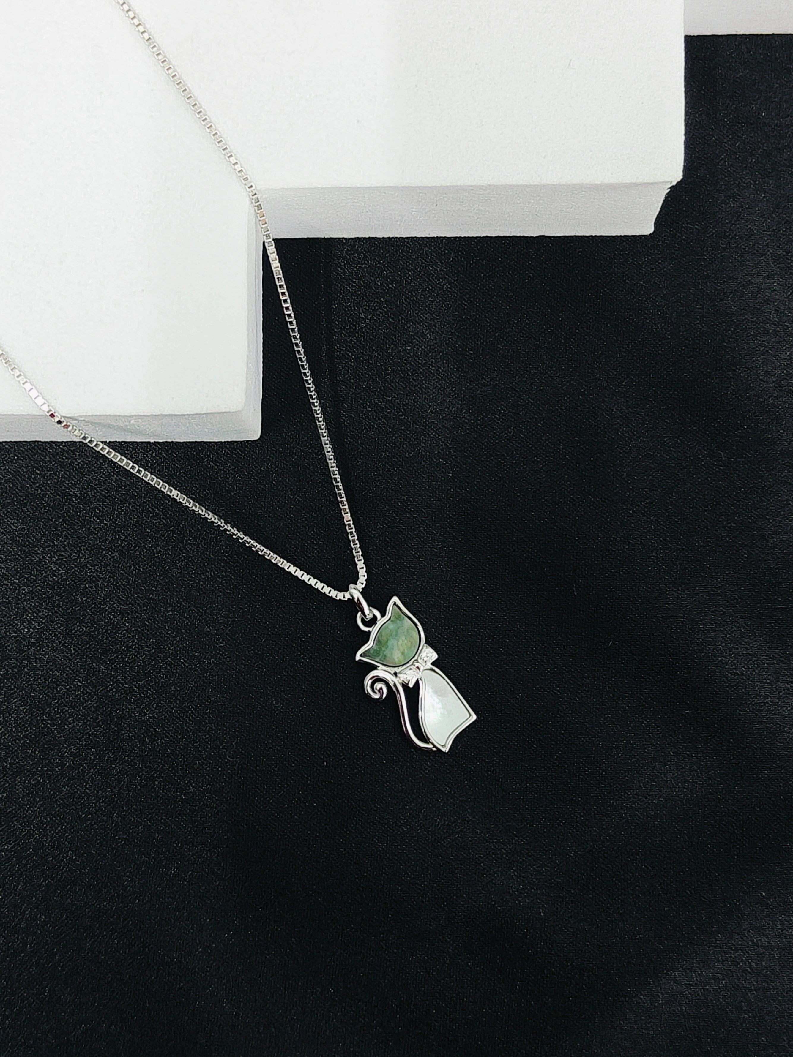 Silver necklace with a cat-shaped pendant on a black surface