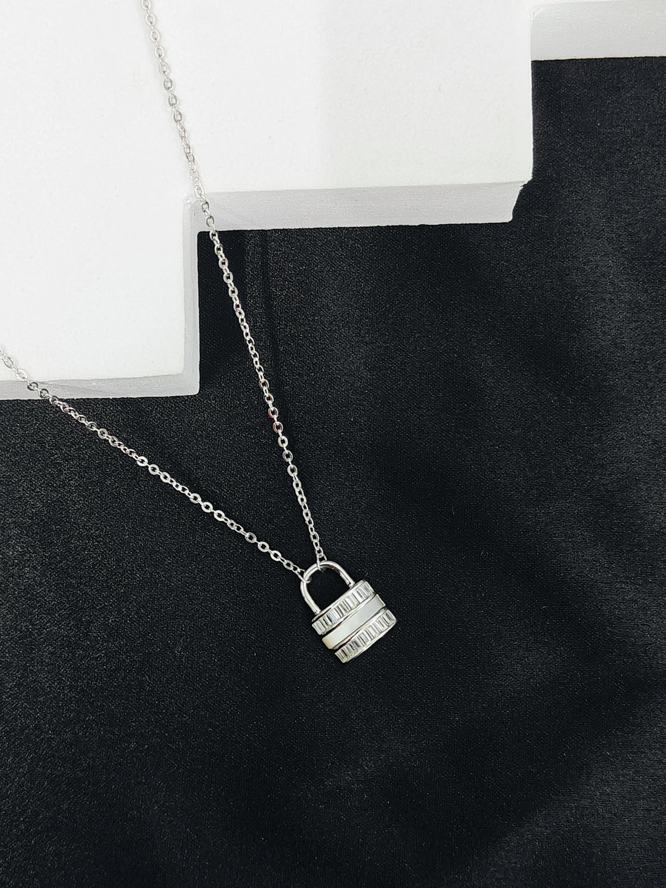 Silver padlock necklace on a black surface with a white box in the background