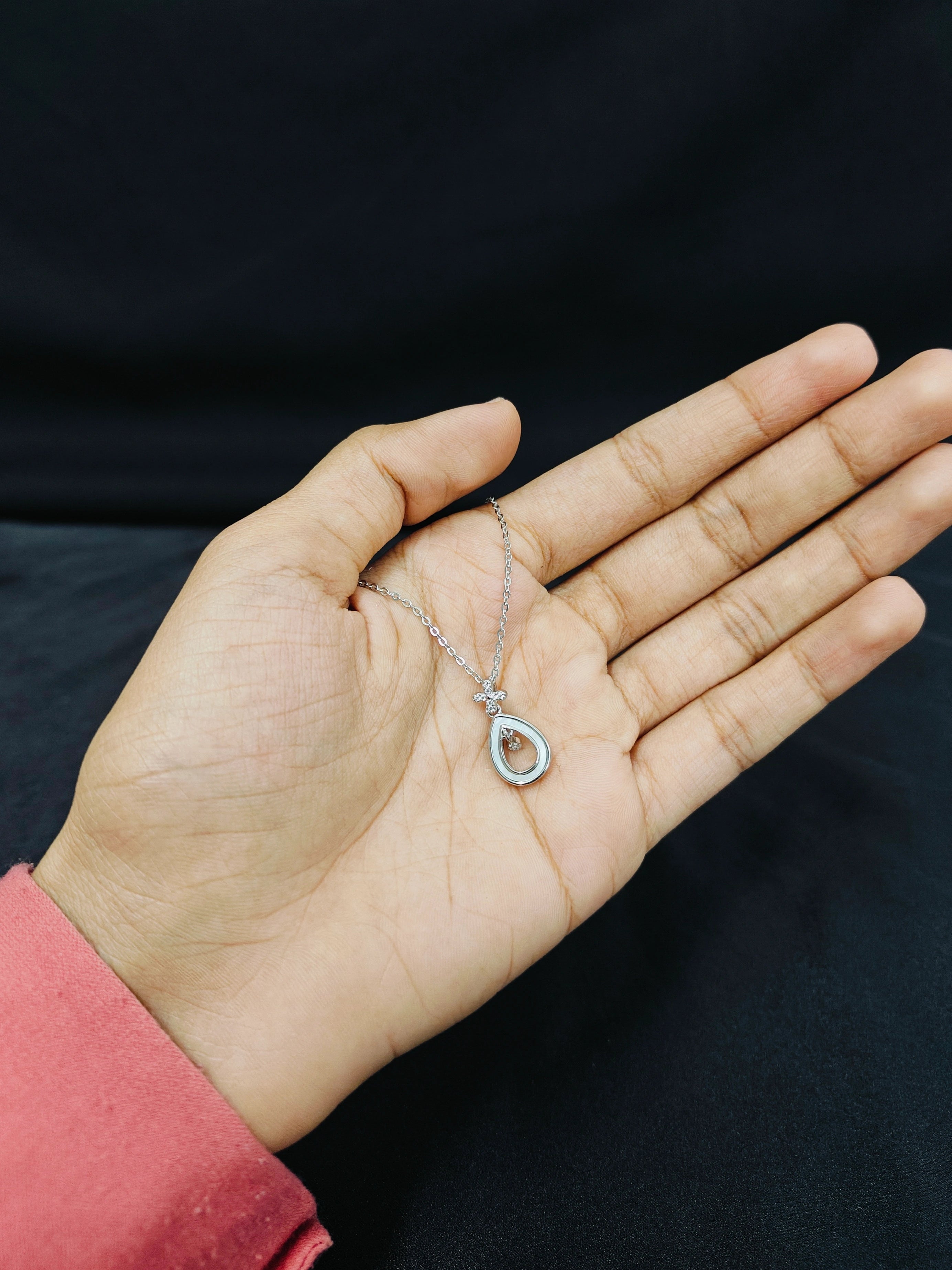 Hand holding a delicate silver necklace with a small pendant against a dark background