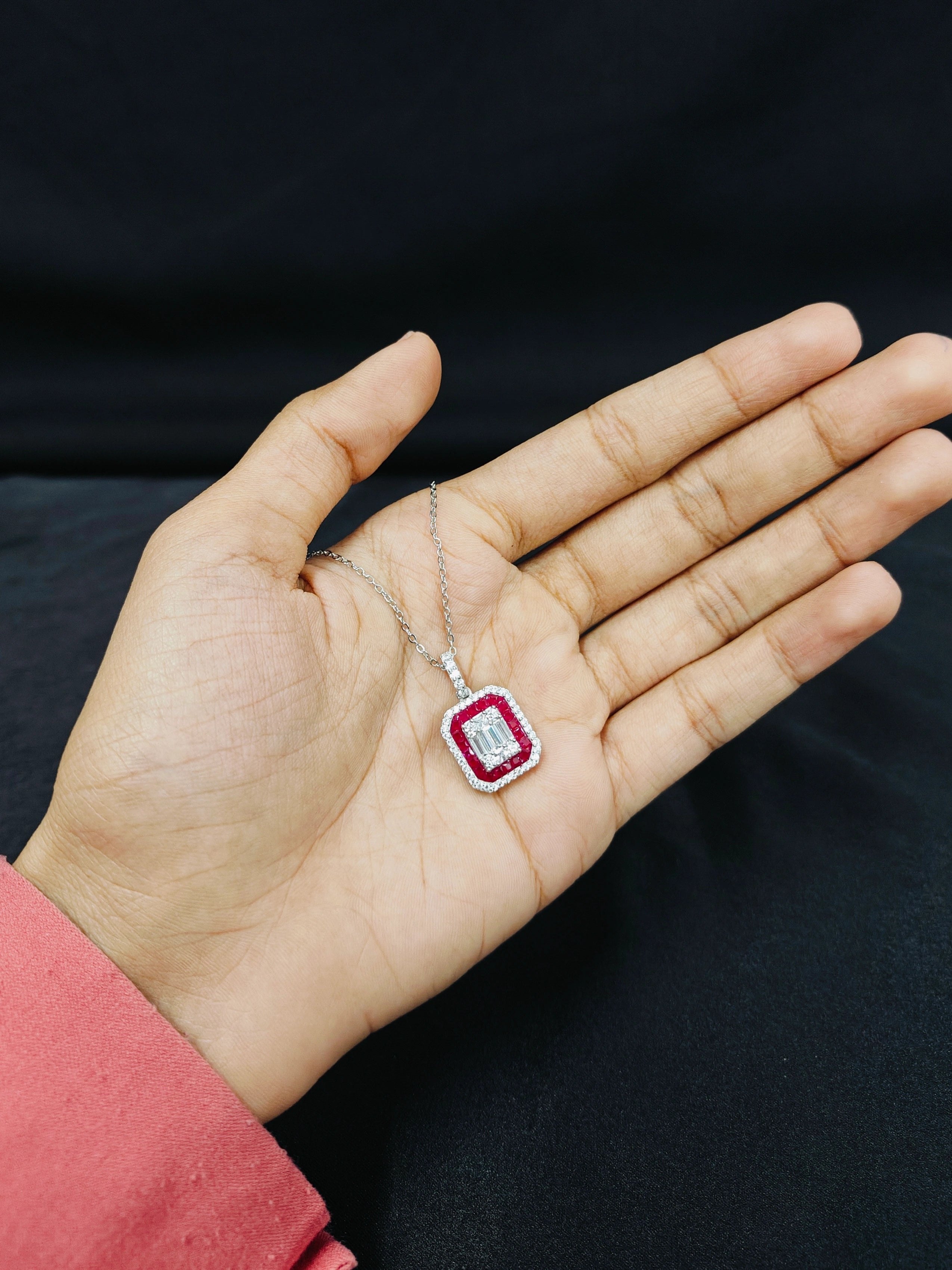 Hand holding a necklace with a red gemstone pendant against a dark background