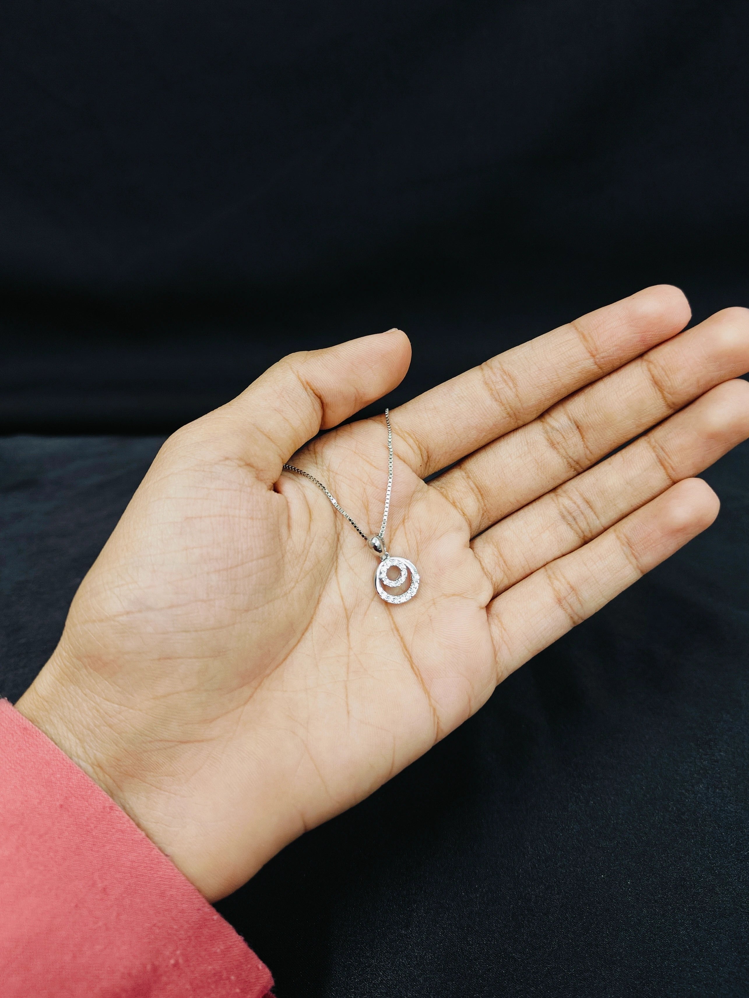 Hand holding a silver necklace with a circular pendant against a black background