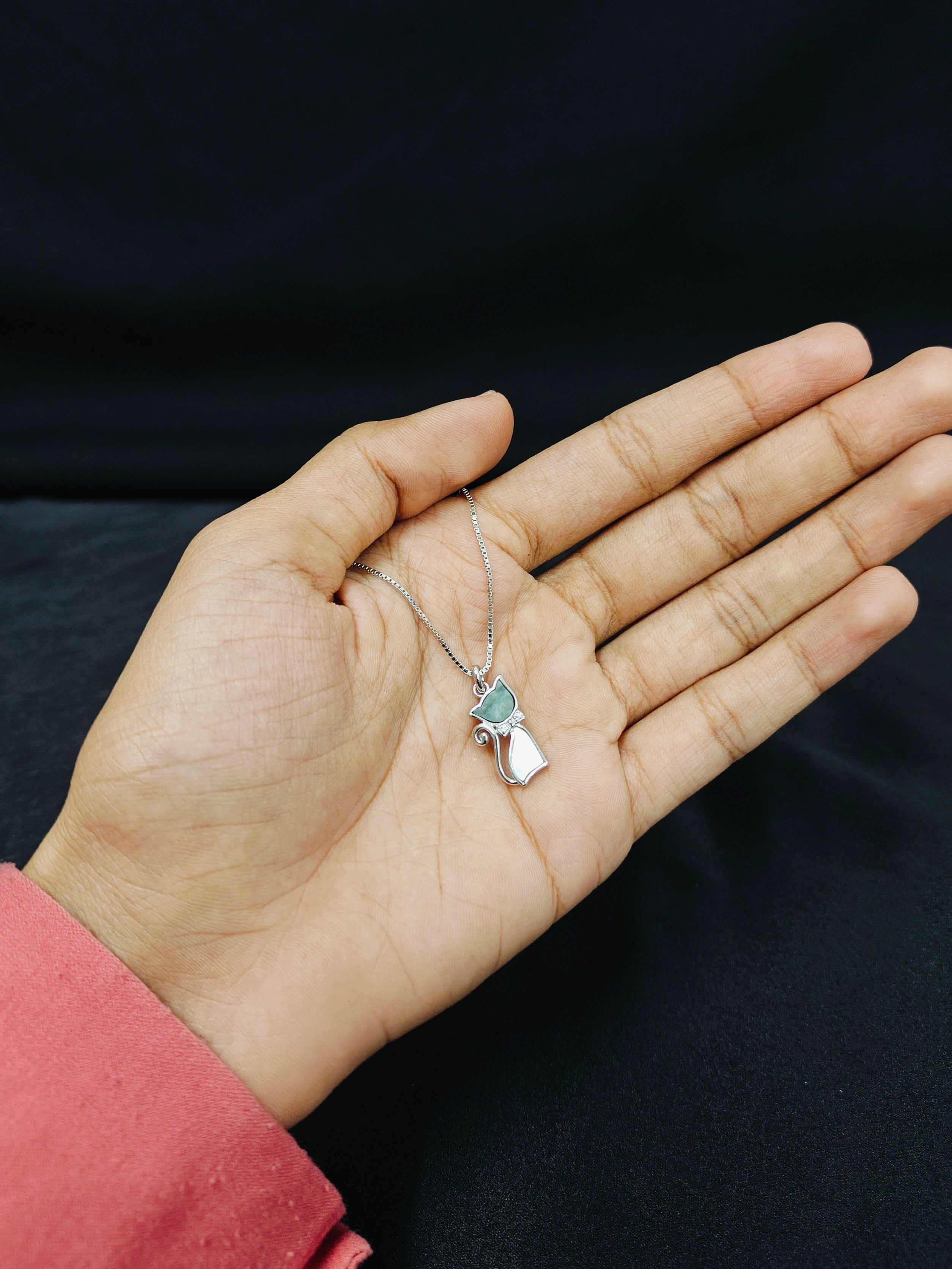 Hand holding a necklace with a pendant against a dark background